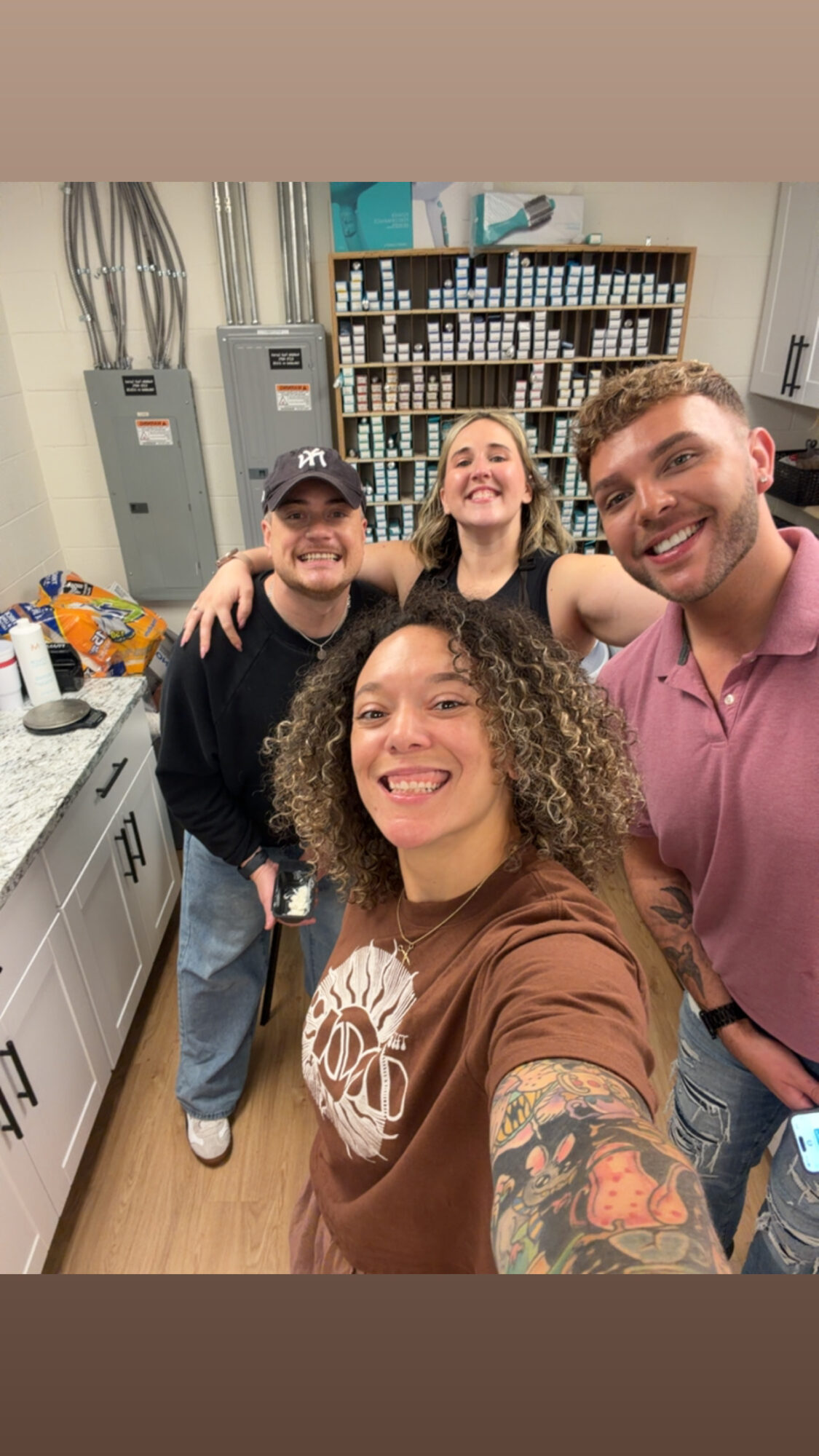 Four people smiling in a room with shelves and cabinets, taking a selfie together.