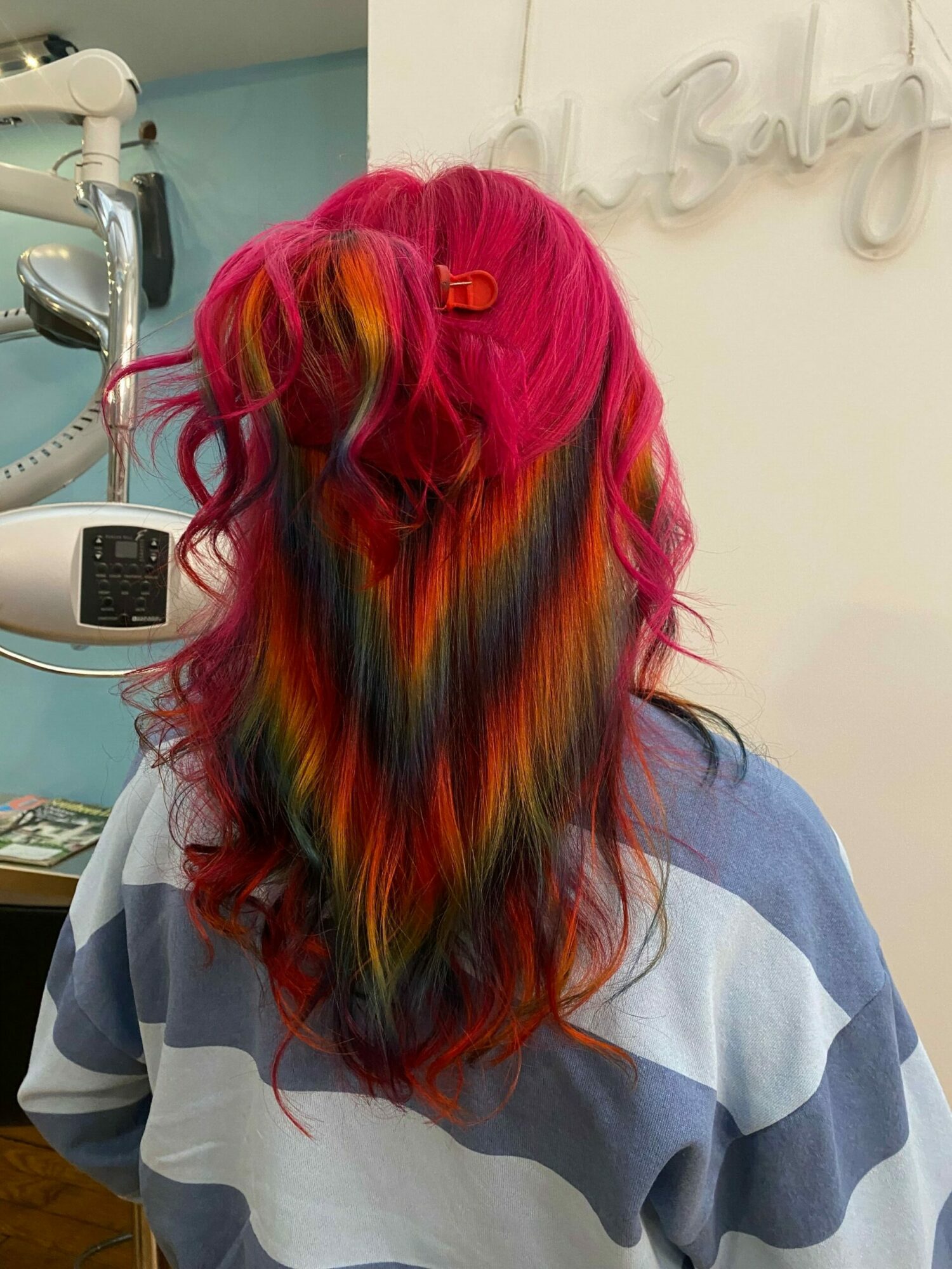 Person with long, colorful hair in shades of pink, red, orange, yellow, and black, wearing a striped shirt.