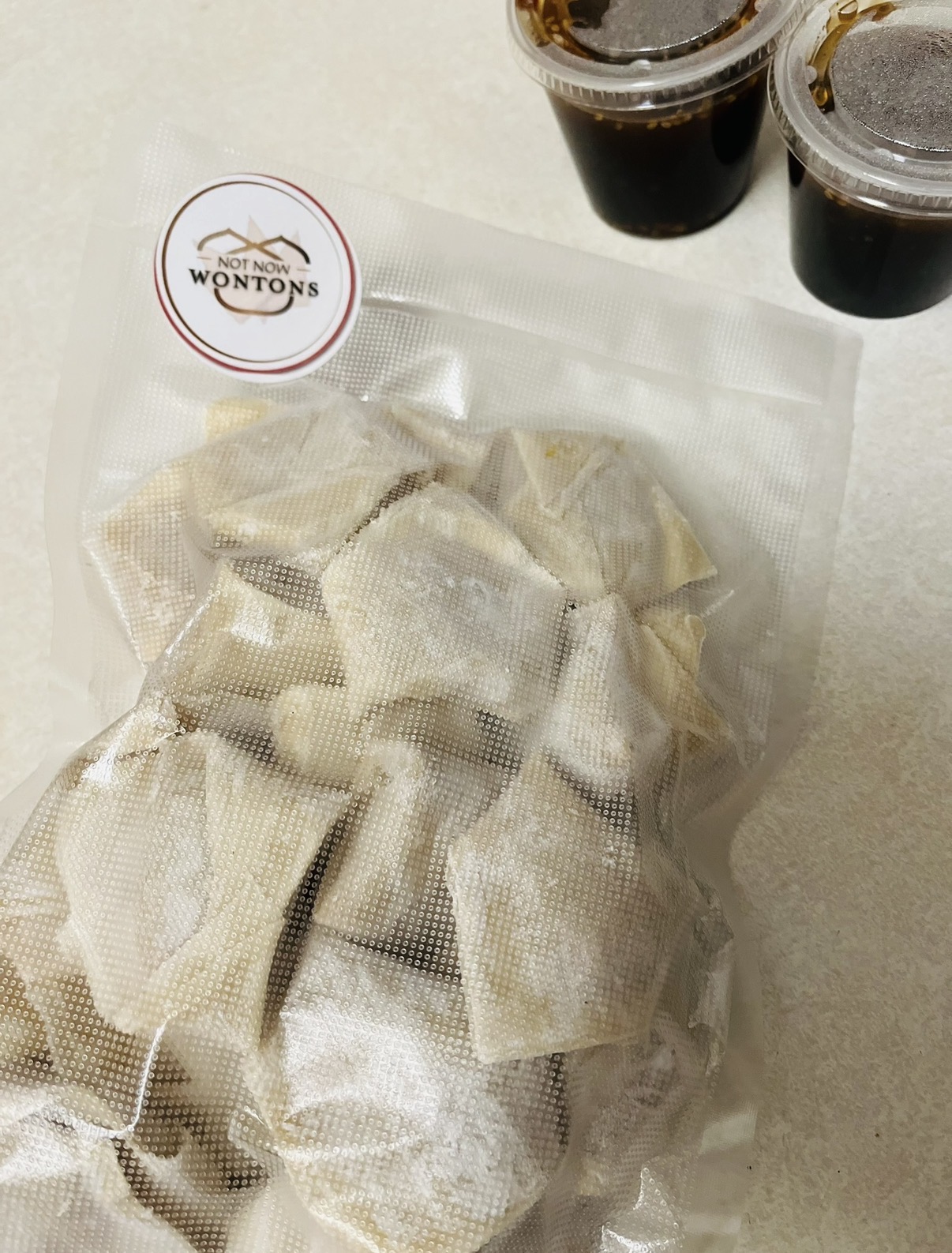 Packaged food items in a clear bag with a label, two cups of dark beverage, on a light surface.