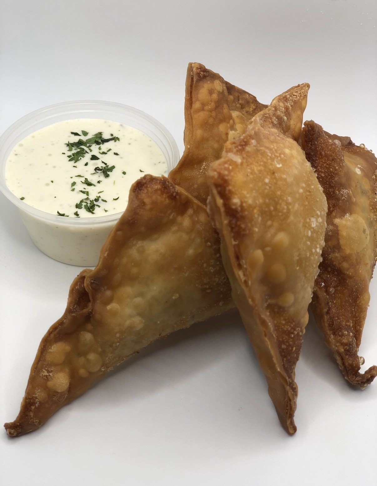Four fried samosas with a small bowl of dipping sauce garnished with herbs, on a white surface.