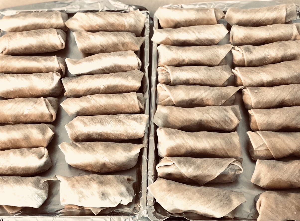 Multiple rows of wrapped food items on trays, arranged in a grid pattern, with a neutral background.