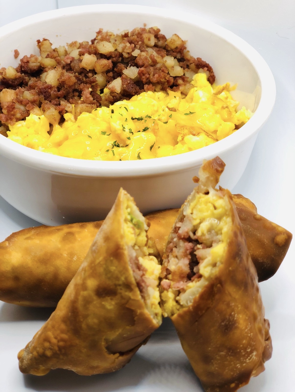 Bowl of scrambled eggs and ground meat with a side of fried spring rolls, one cut open showing filling.