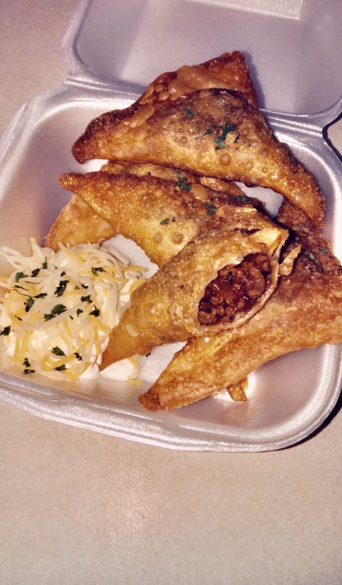 Fried empanadas with a side of rice and herbs in a takeout container.