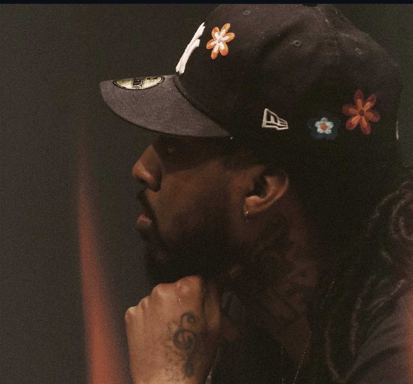 Side profile of a person wearing a black cap with floral decorations, resting their chin on their hand.