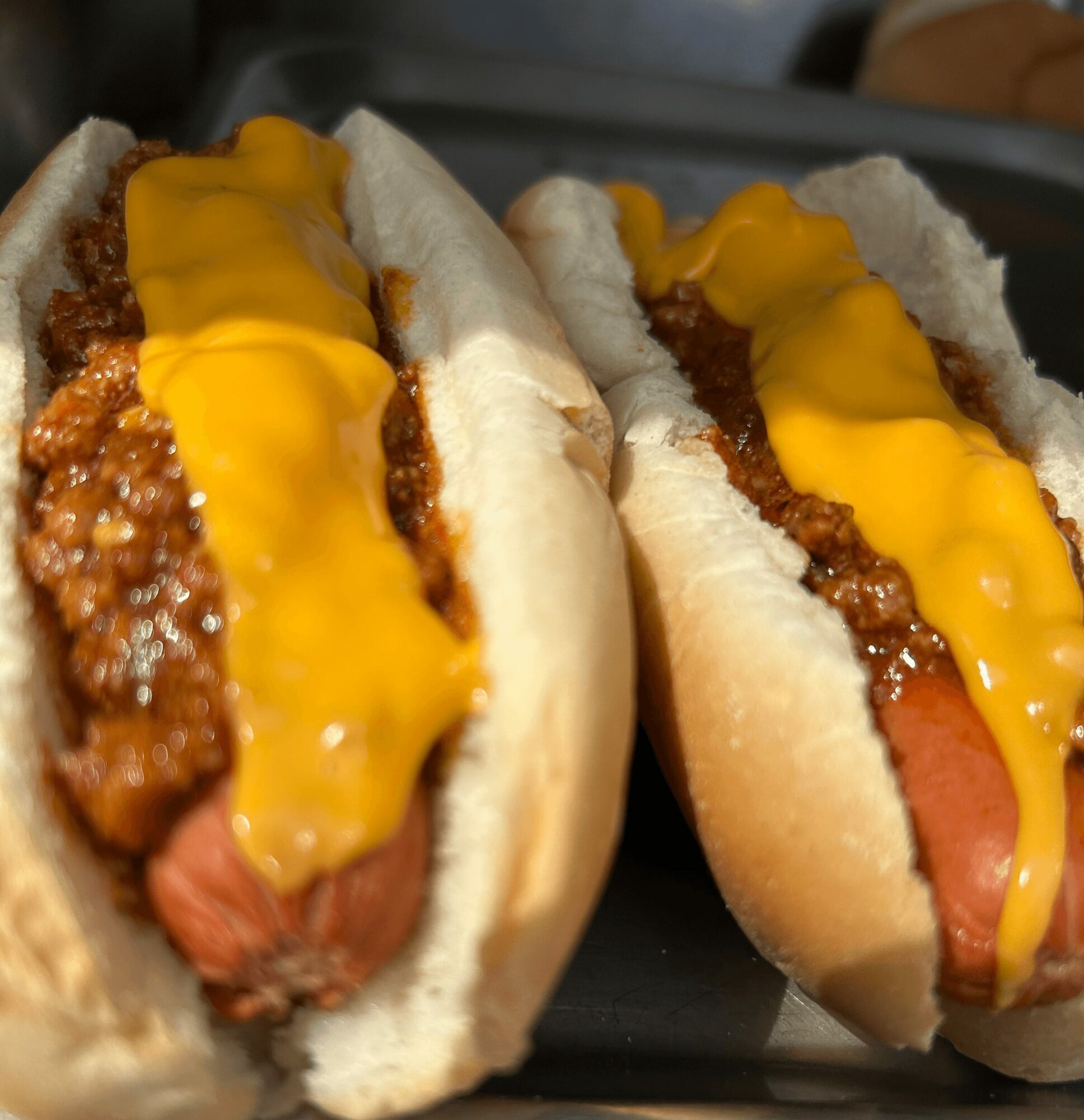 Two hot dogs with chili and melted cheese in buns on a black plate.