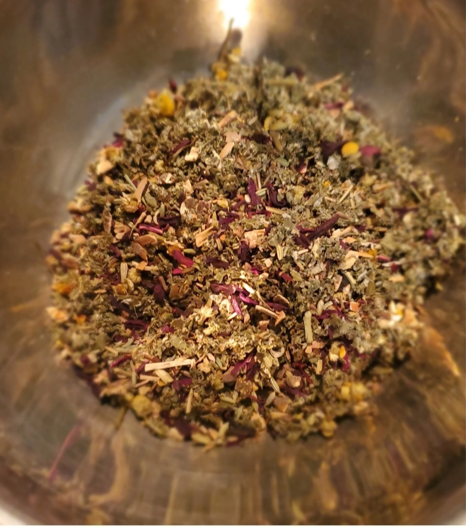 Mixed dried herbs and flower petals in a container, with a variety of colors and textures, viewed from above.