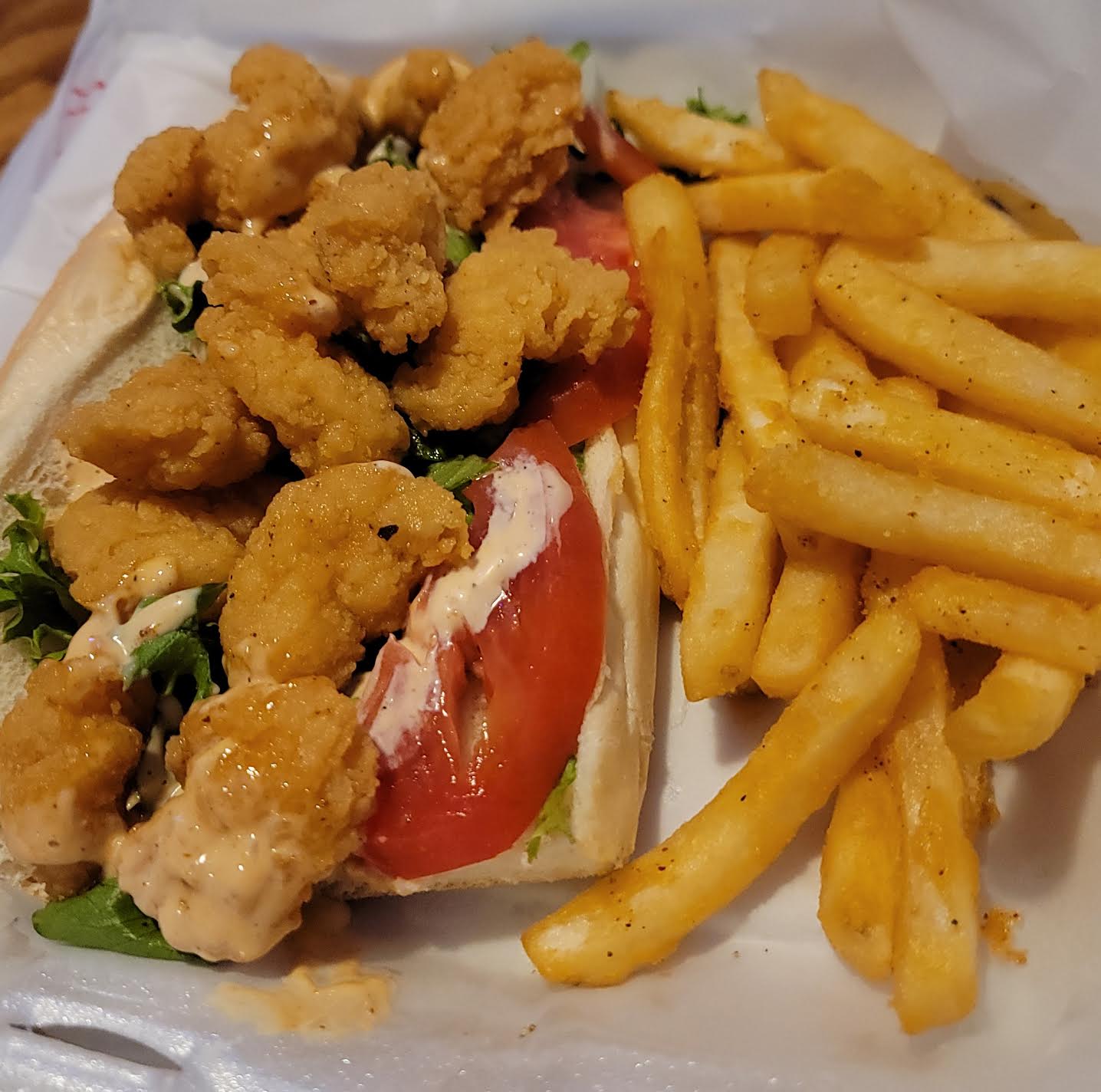 Fried chicken pieces, tomato, lettuce in a sandwich bun, and French fries on a tray.