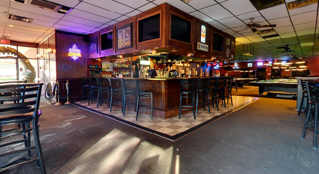 Bar with high chairs, illuminated screens, and tables in a dimly lit setting.