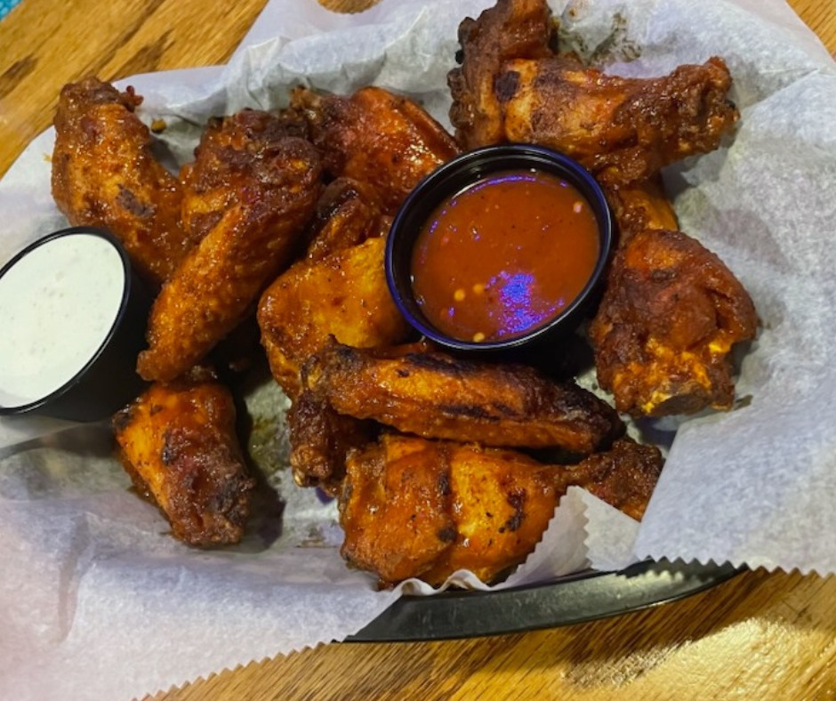 Basket of fried chicken wings with dipping sauces on parchment paper, on a wooden surface.