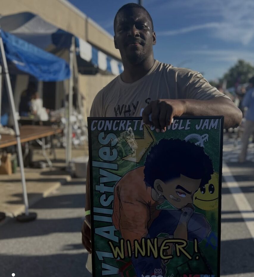 Person holding a colorful sign with a cartoon character and the word 'WINNER' outdoors on a sunny day.