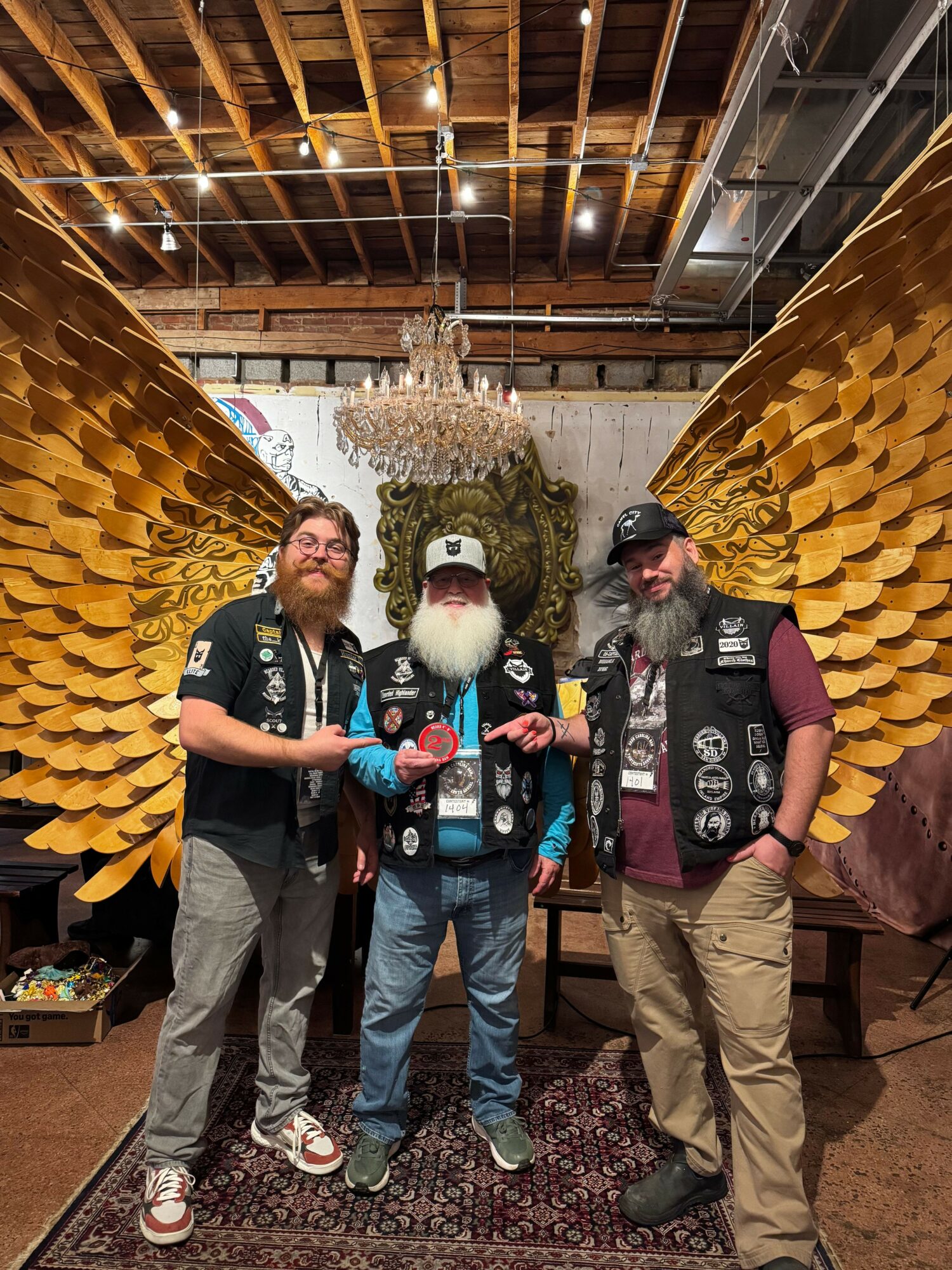 Four people stand together indoors, with large golden wings and a chandelier overhead, posing for a photo.