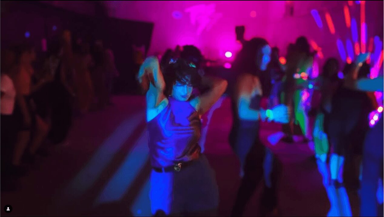 People dancing in a nightclub with colorful lighting and a dark background.
