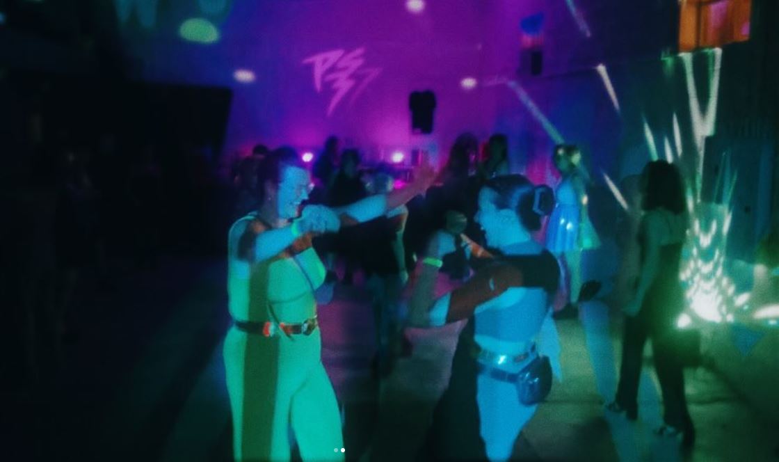 People dancing in a dark room with colorful lights and projections, enjoying a party or dance event.