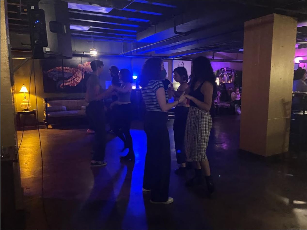 People dancing and socializing in a dimly lit nightclub with colorful lighting and a relaxed atmosphere.