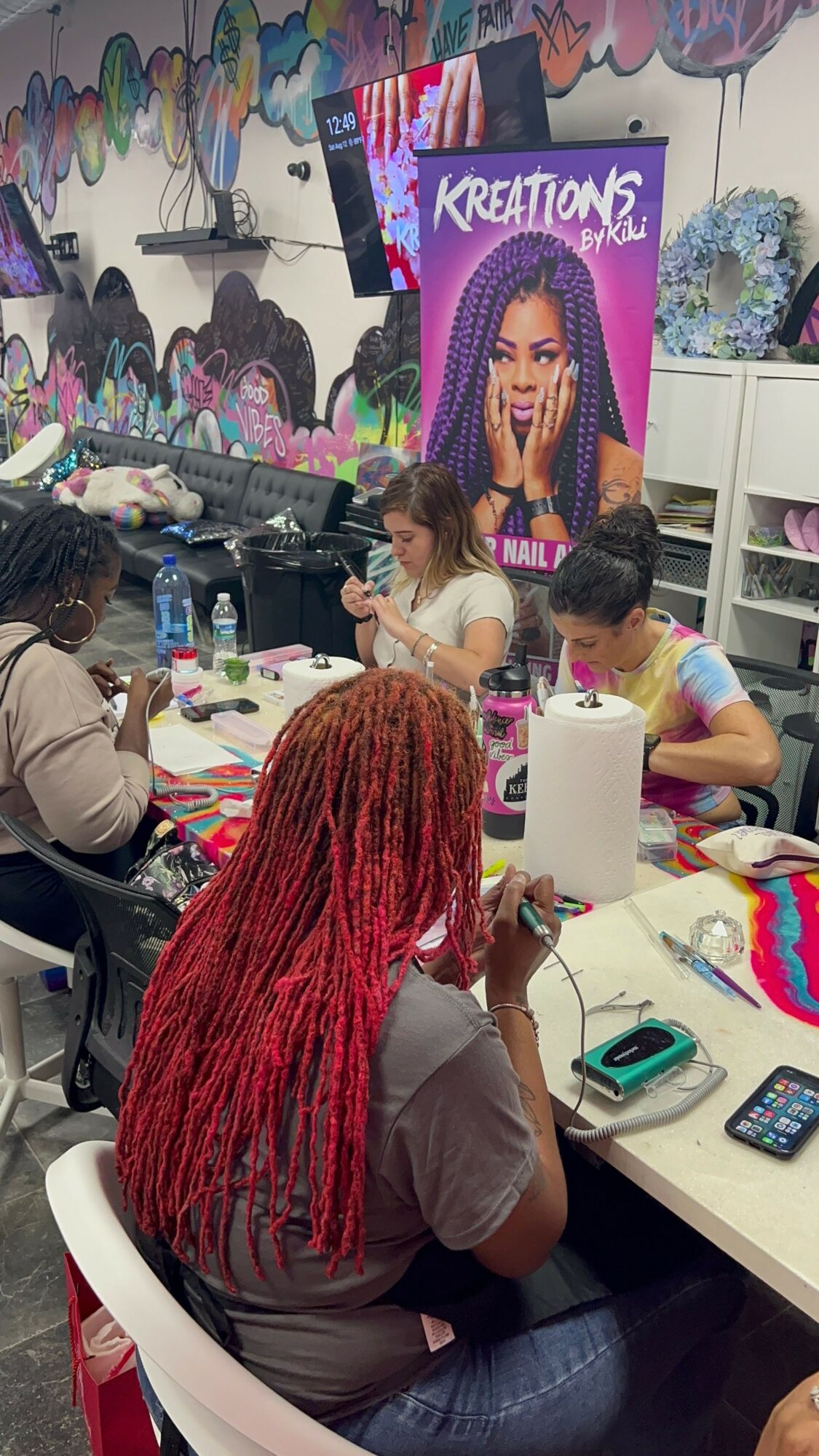 People gathered around a table with colorful decorations and a cake, in a room with vibrant wall art and a banner.