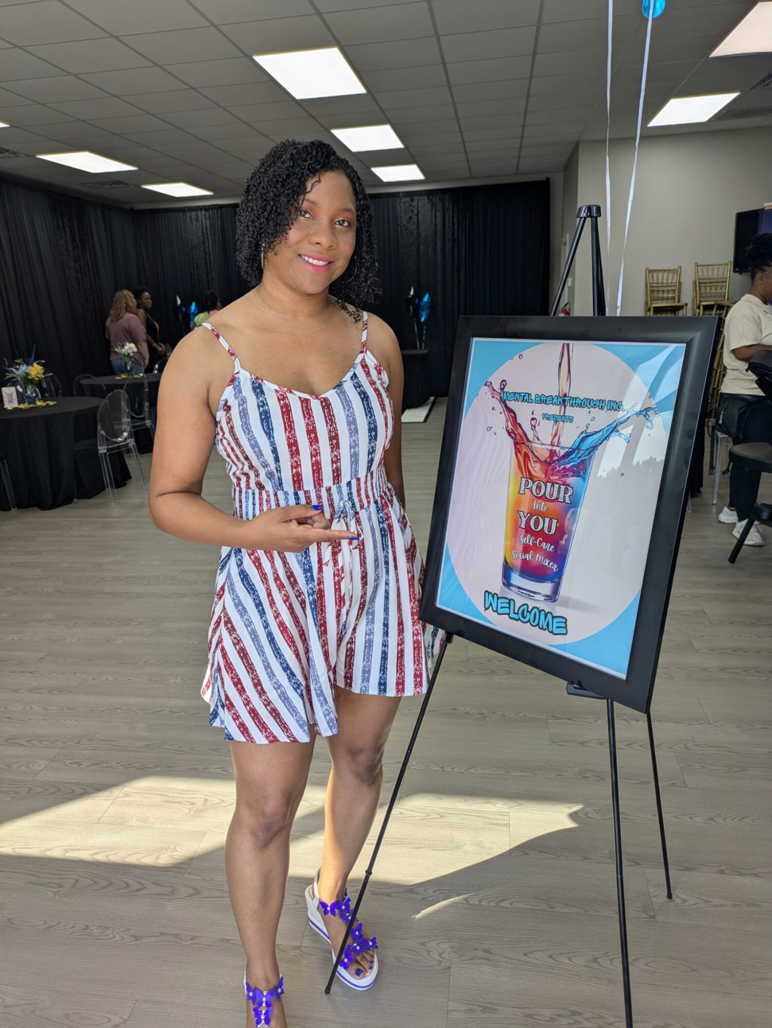 Young woman in striped dress standing next to a colorful poster display in an indoor event space.