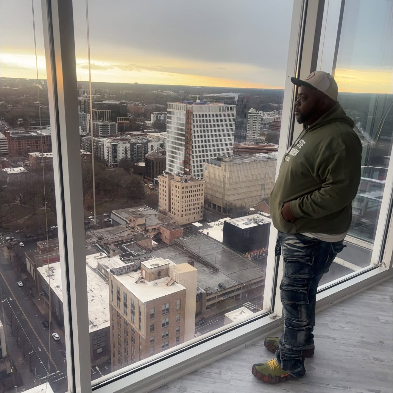 Man standing inside a high-rise building looking out at cityscape through large glass windows.