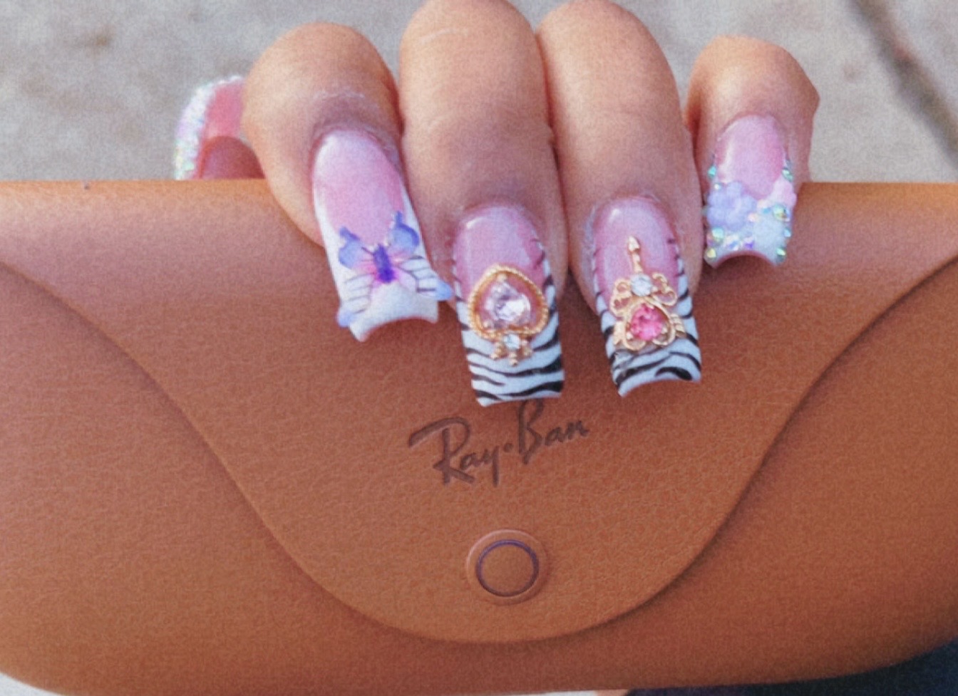 Hand with decorated nails holding a tan purse with a
