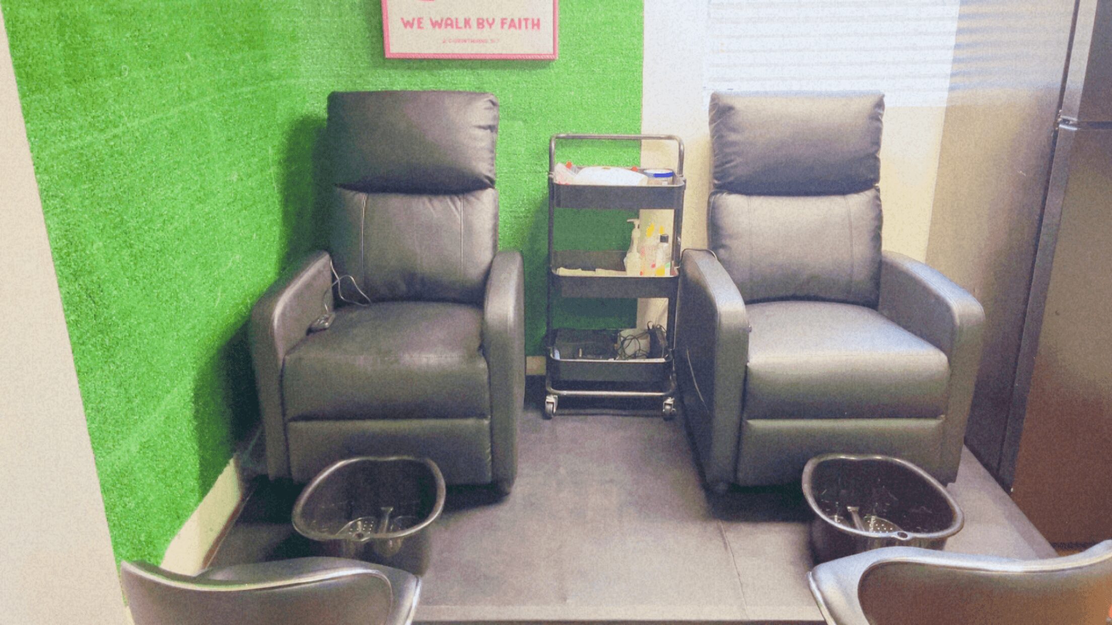 Two gray recliner chairs with footrests and a small table between them, in a room with green wall and window blinds.