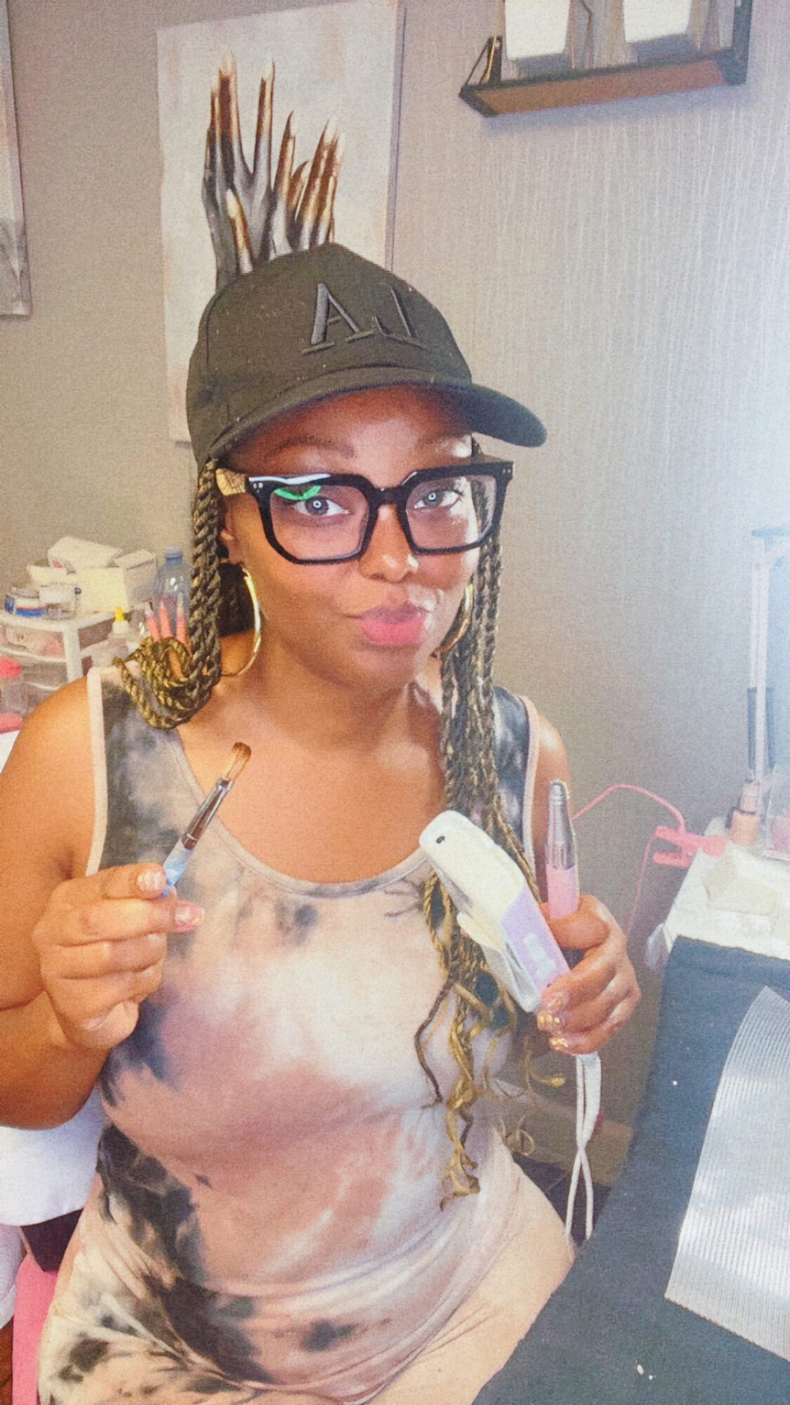 Woman wearing glasses and a cap, holding a small animal and a device, sitting at a desk in a room.