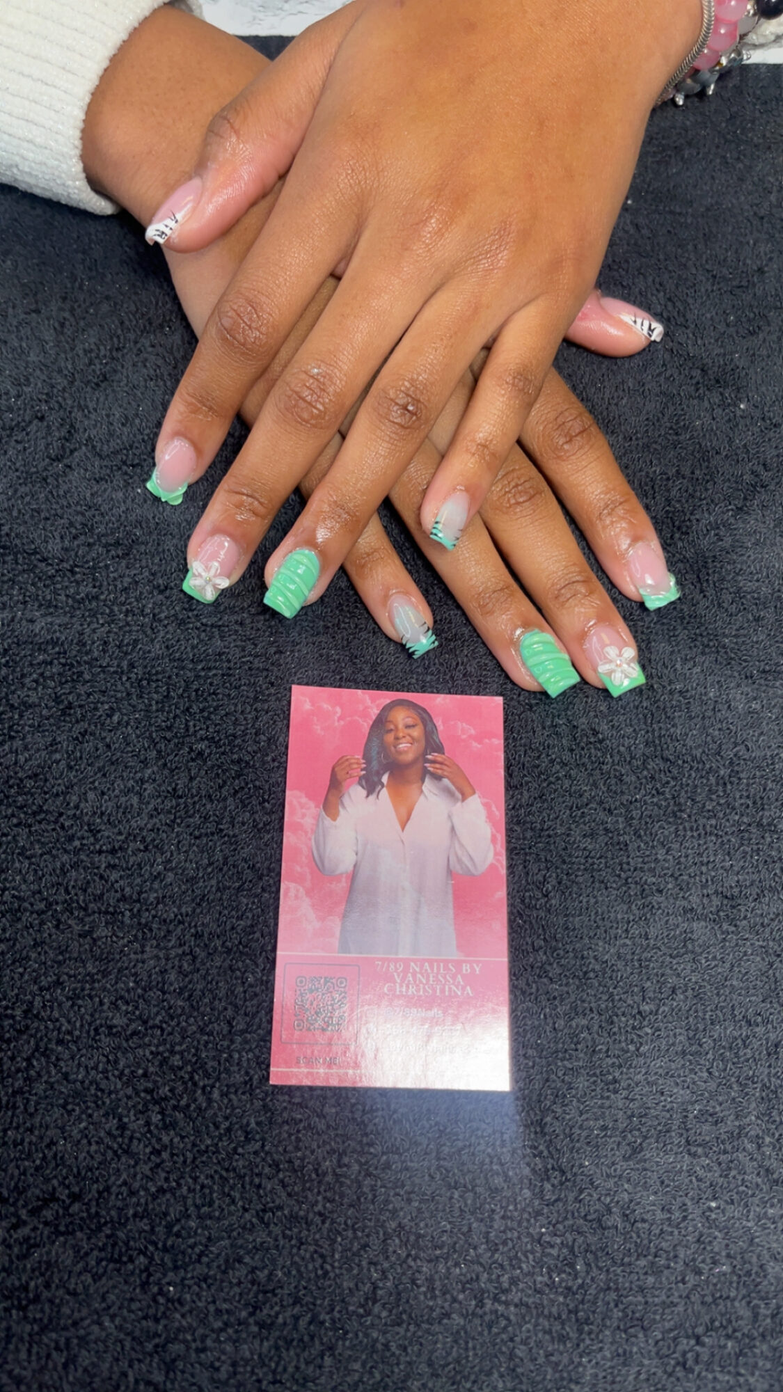 Two hands with manicured nails resting on a dark surface, with a pink card featuring a woman in a white outfit below.