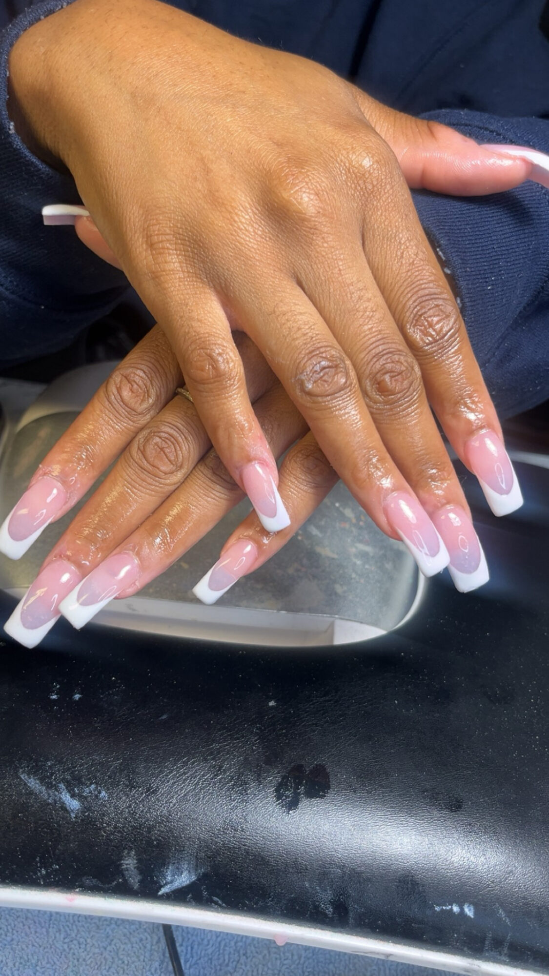 Two hands with long, manicured nails resting on a surface, with a focus on the nails and skin texture.