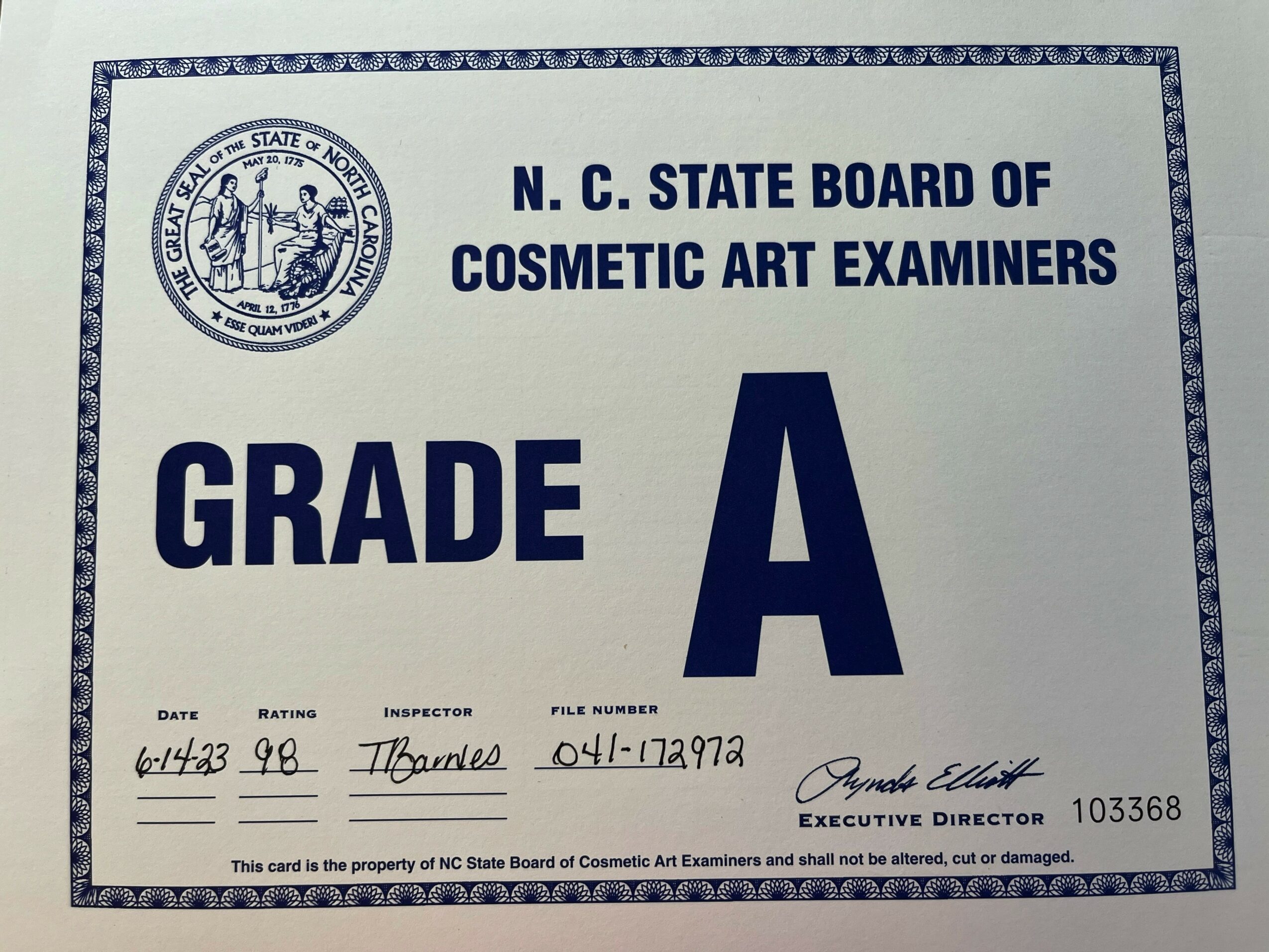 Certificate from North Carolina State Board of Cosmetic Art Examiners with grade A, date, inspector, and signature.
