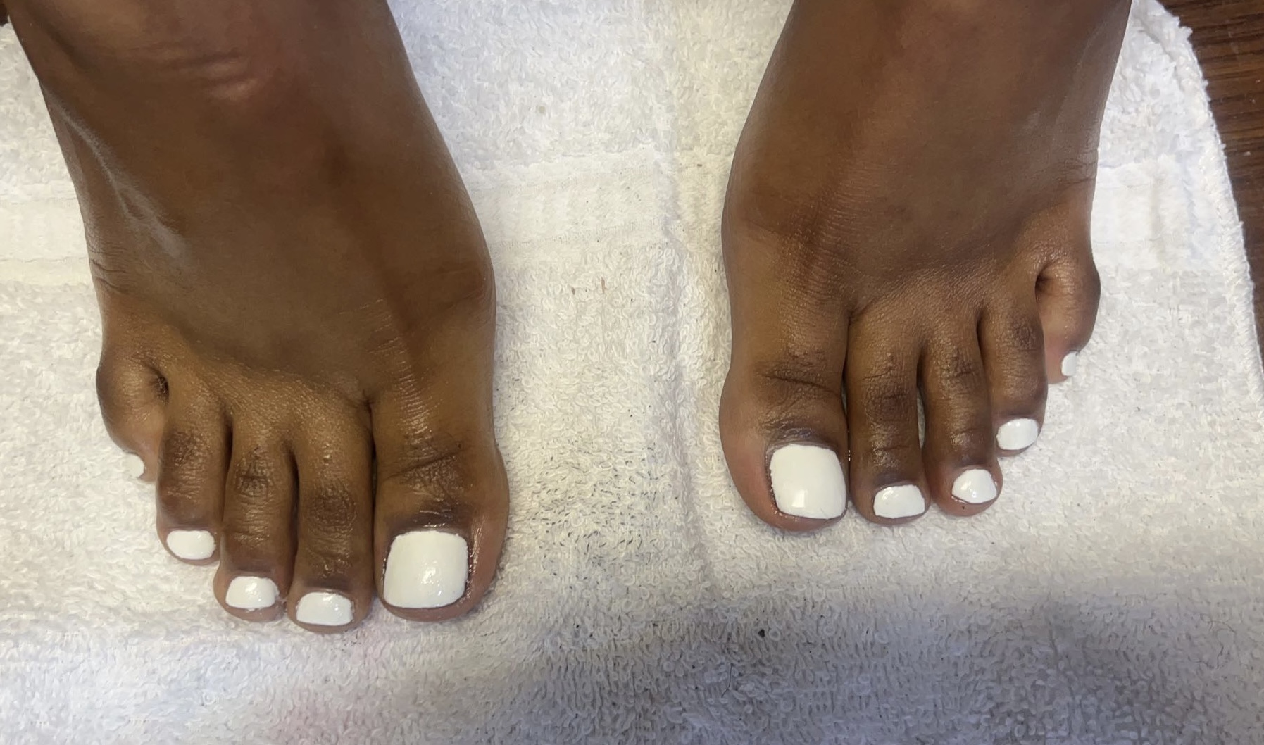 Two feet with white painted toenails resting on a towel, toes slightly spread apart.