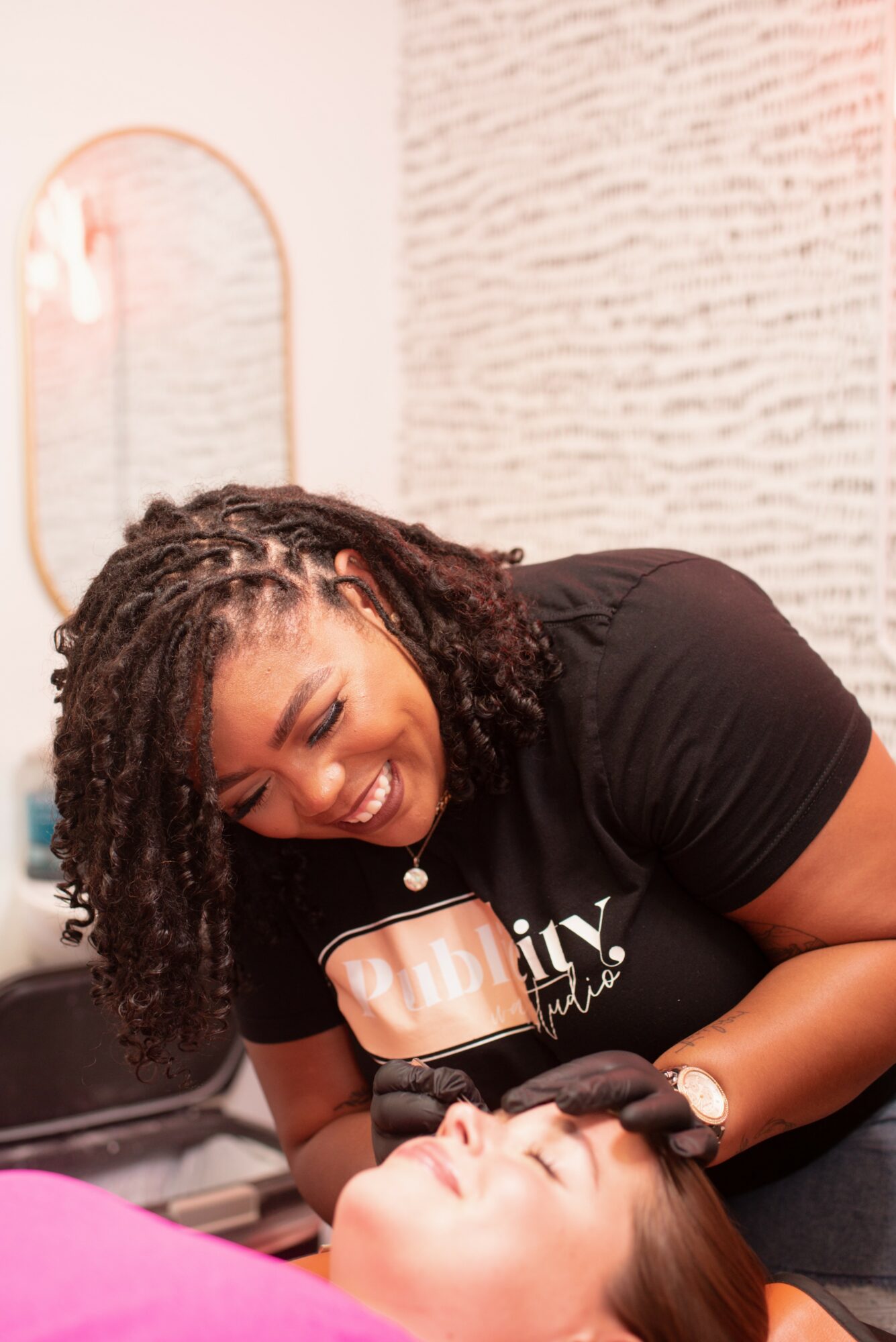 A woman with curly hair smiling and leaning over a person lying down in a room with a mirror and textured wall.