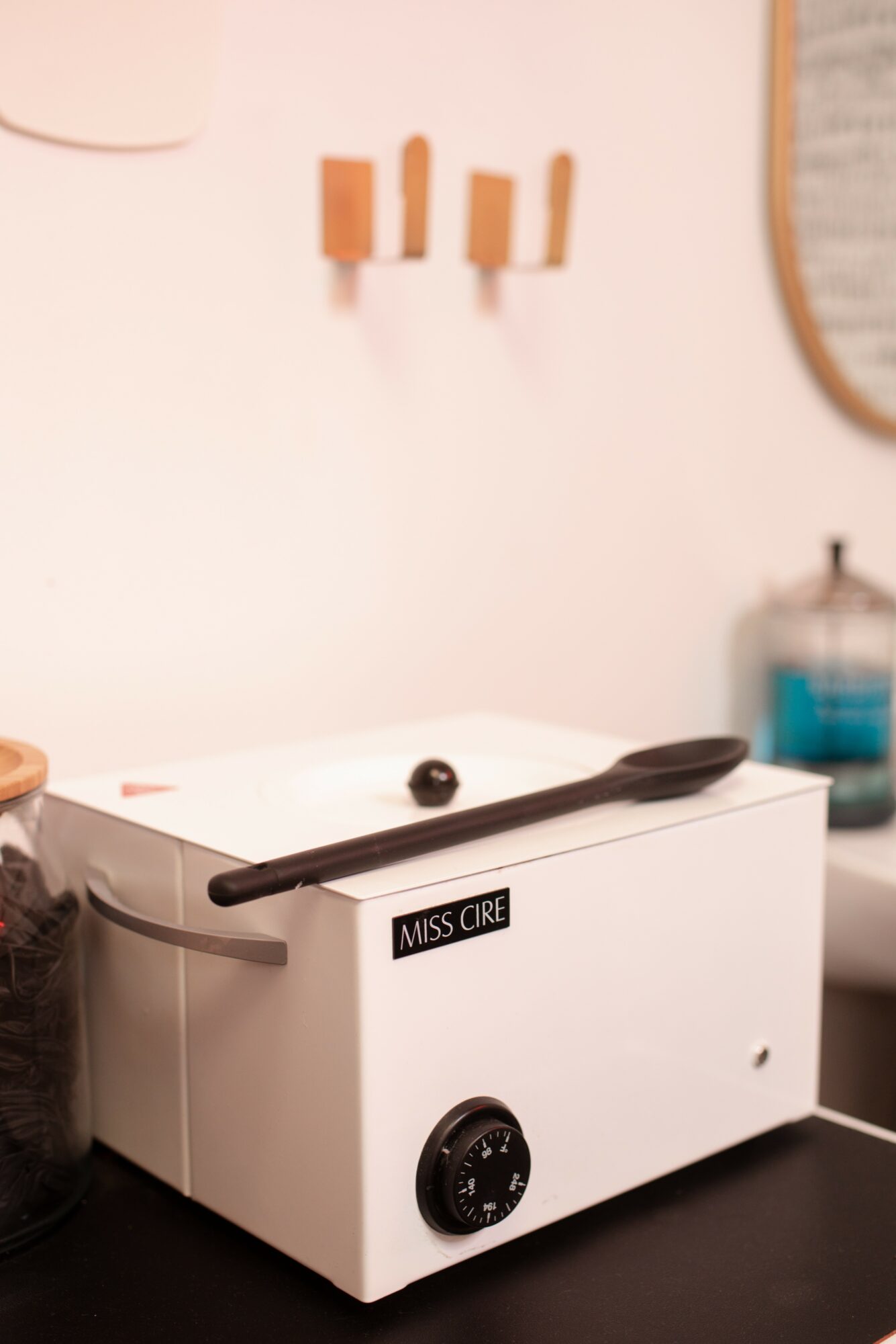 A white sterilizer machine with a black handle and control dial on a black surface, with a wall and mirror in the background.