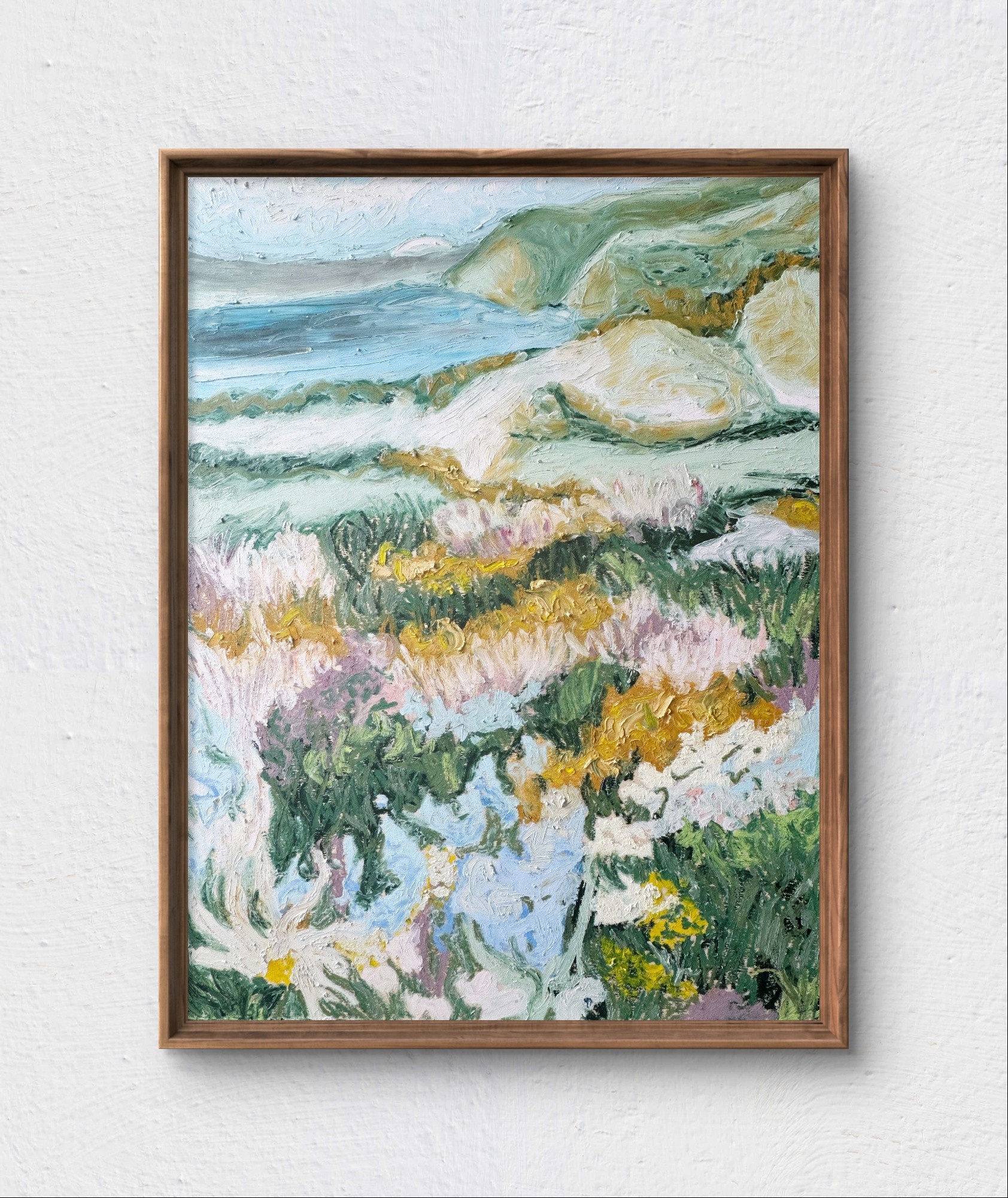 Landscape painting of a coastal scene with rocks, waves, and colorful flowers in the foreground, framed and hung on a wall.