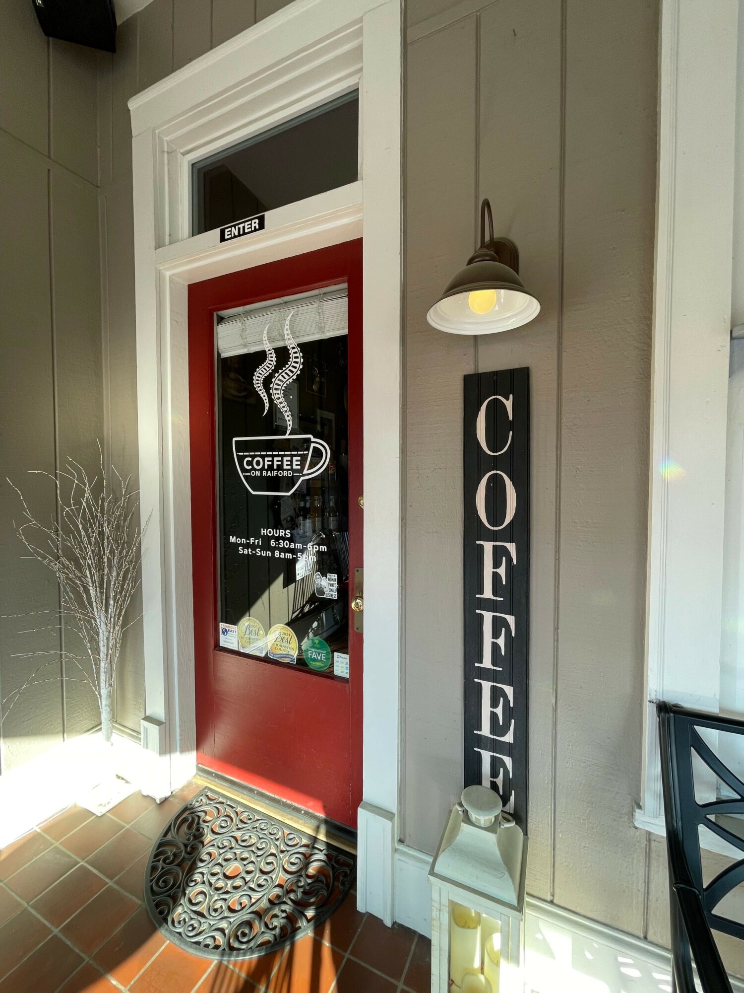 Door with a sign, window, and decorative elements inside a building, with a patterned floor and a plant. Word on sign is unclear.