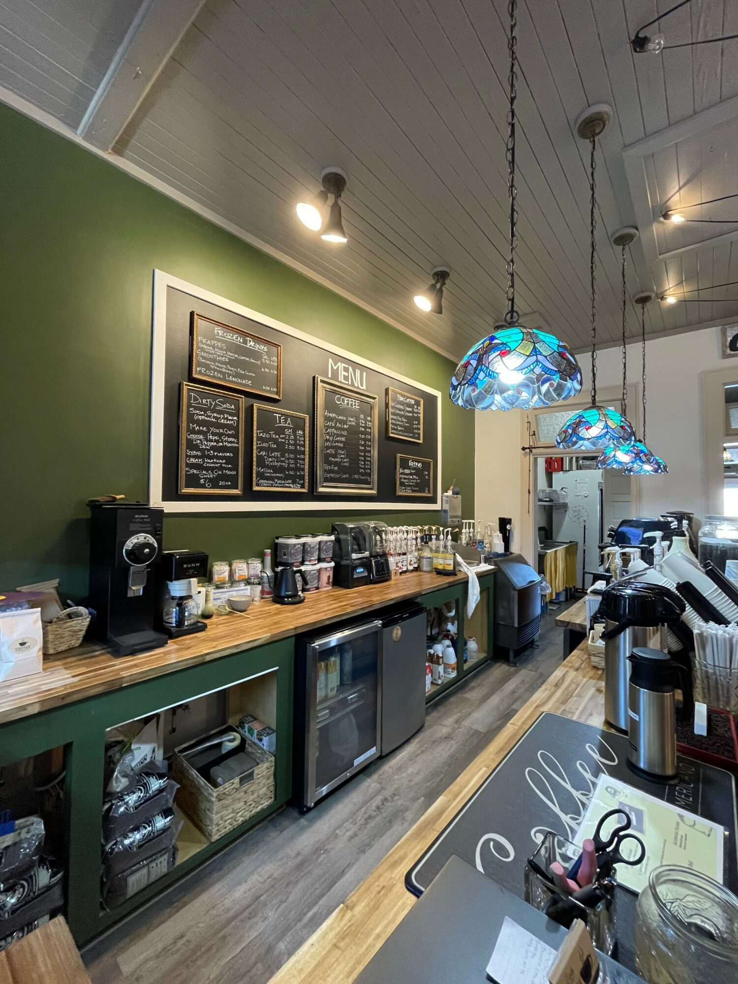 Coffee shop interior with hanging blue pendant lights, chalkboard menus, and a wooden counter with coffee equipment.