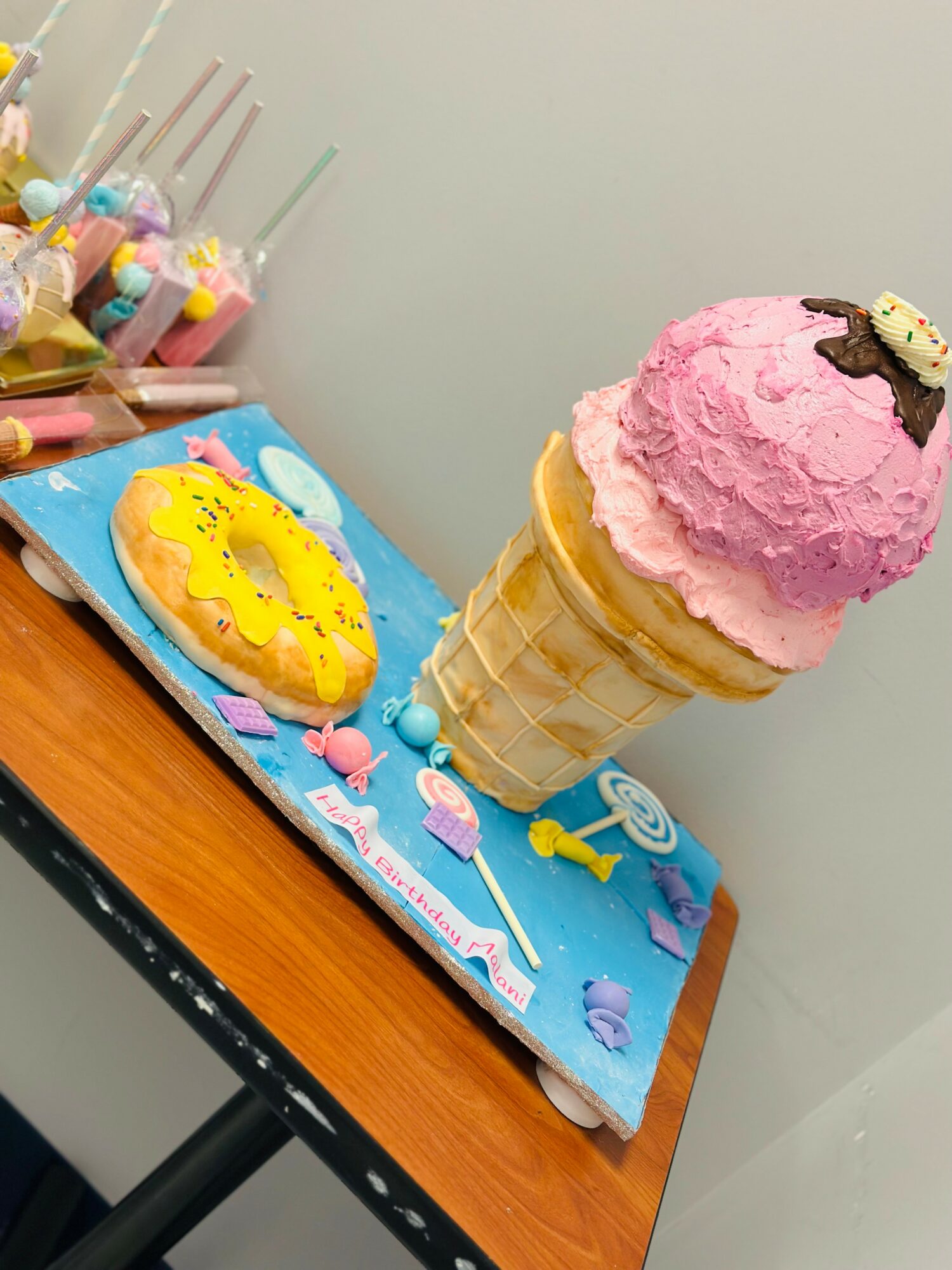 Ice cream cone with pink and purple scoops on a table with colorful decorations and a blue background.