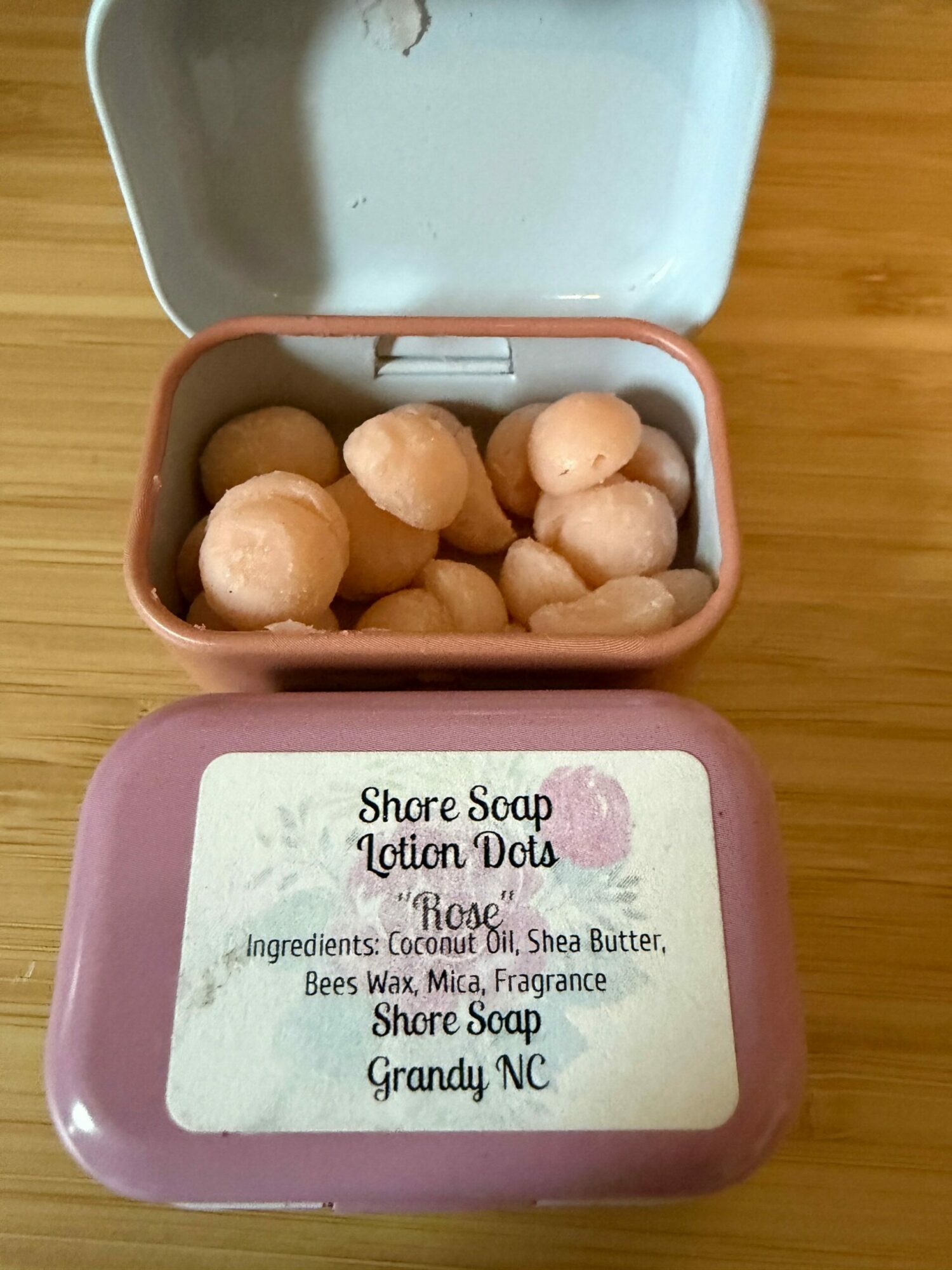 Open soap container with round soap pieces inside, pink soap box with label, wooden surface background.