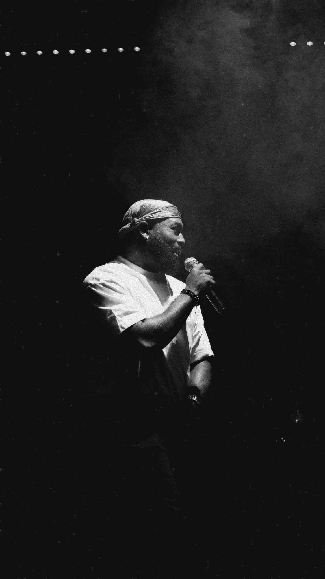 Person holding microphone on stage, illuminated by light, dark background, smoke or fog, black and white image.