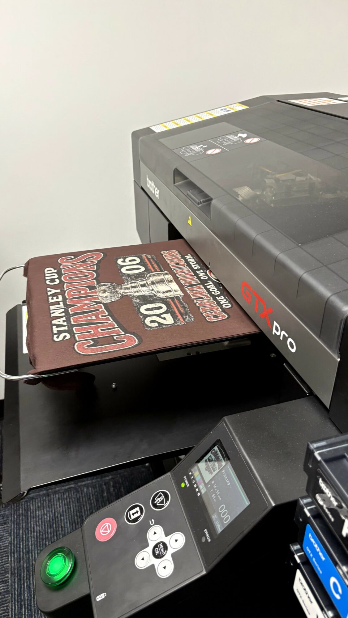 Printer with a sign reading 'STANLEY CUP CHAMPIONS 2020' leaning against it, on a black surface, with a control panel nearby.