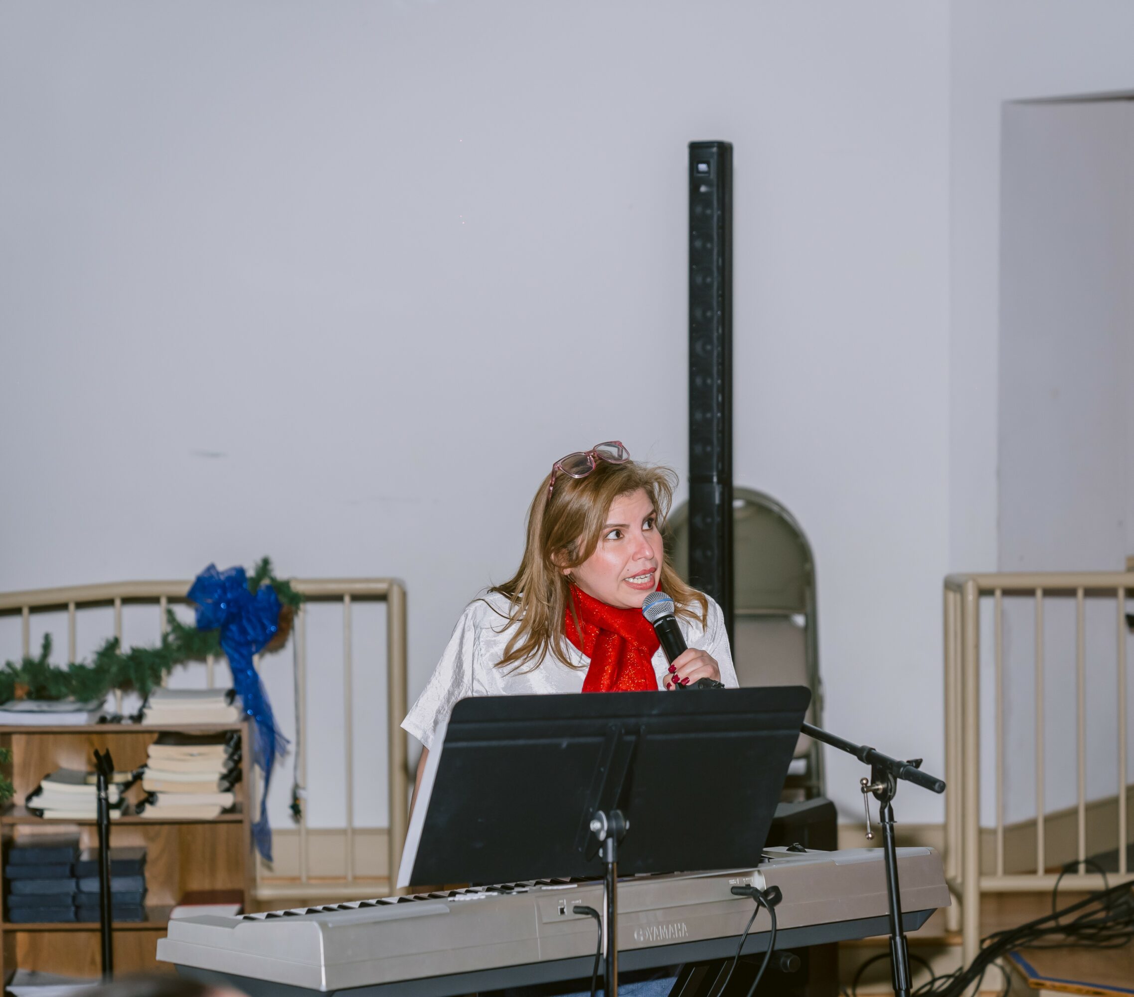 Woman singing into a microphone at a keyboard, with a music stand and a height measurement chart behind her.