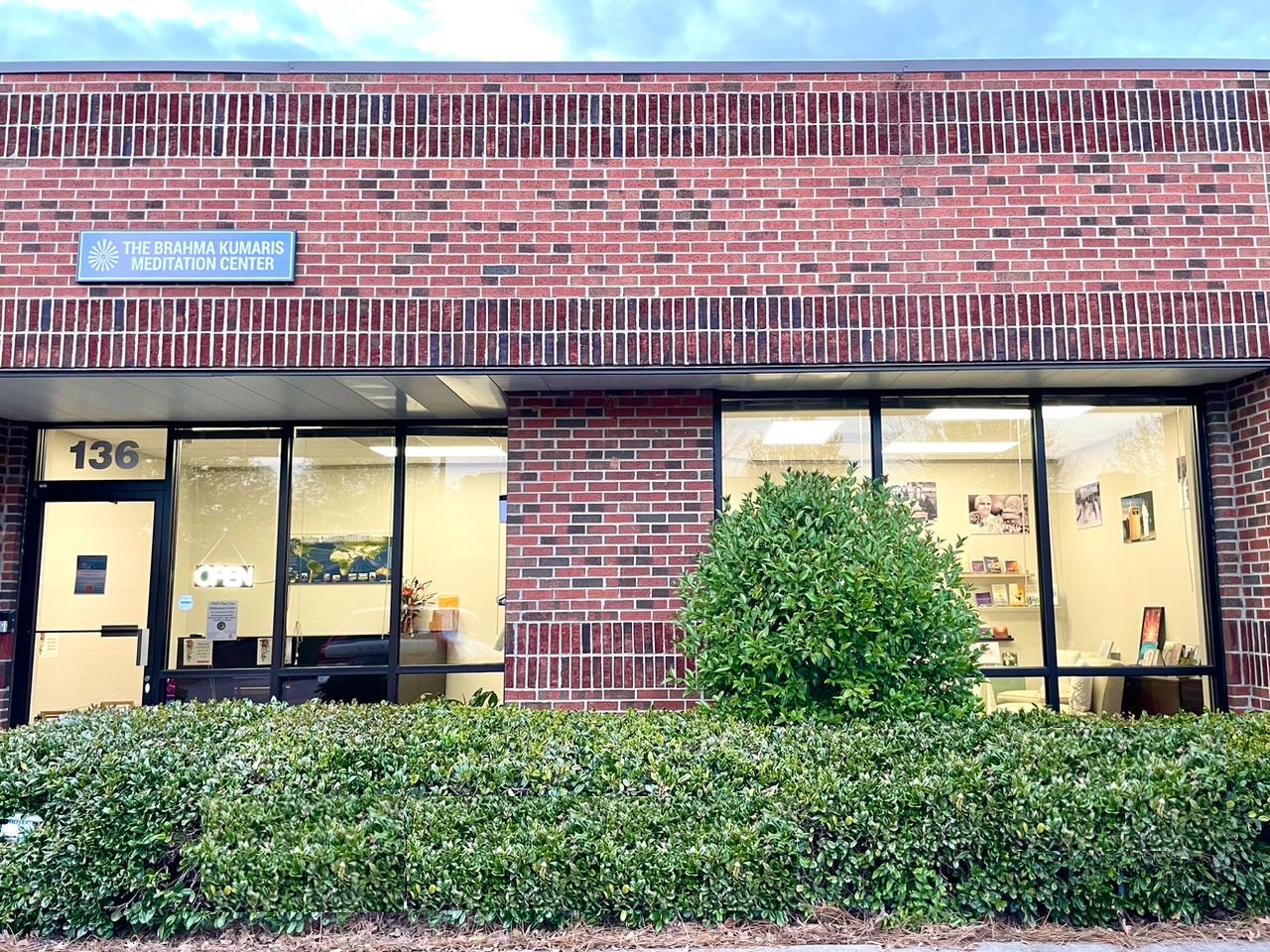 Brick building with large windows, a bush in front, and a blue sign on the upper left corner.