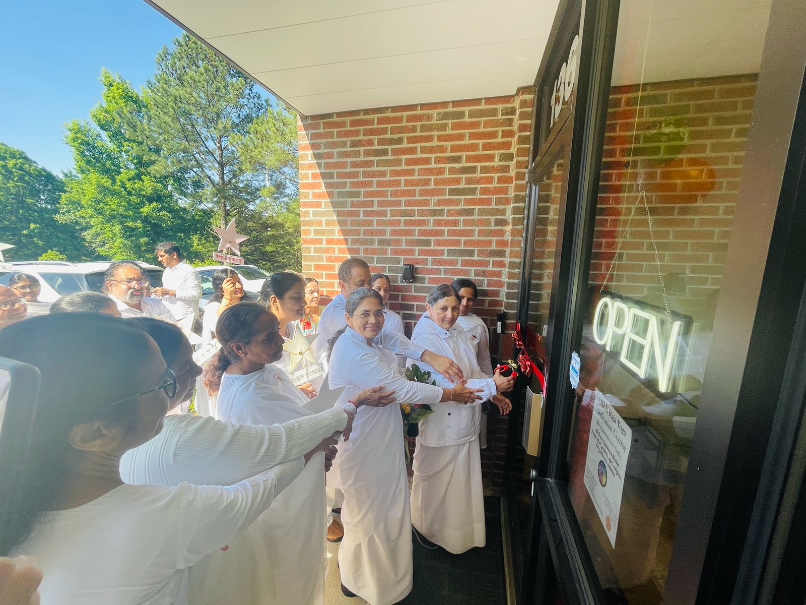 Group of women in white dresses standing outside near a brick building, holding candles, participating in a ceremony or event.