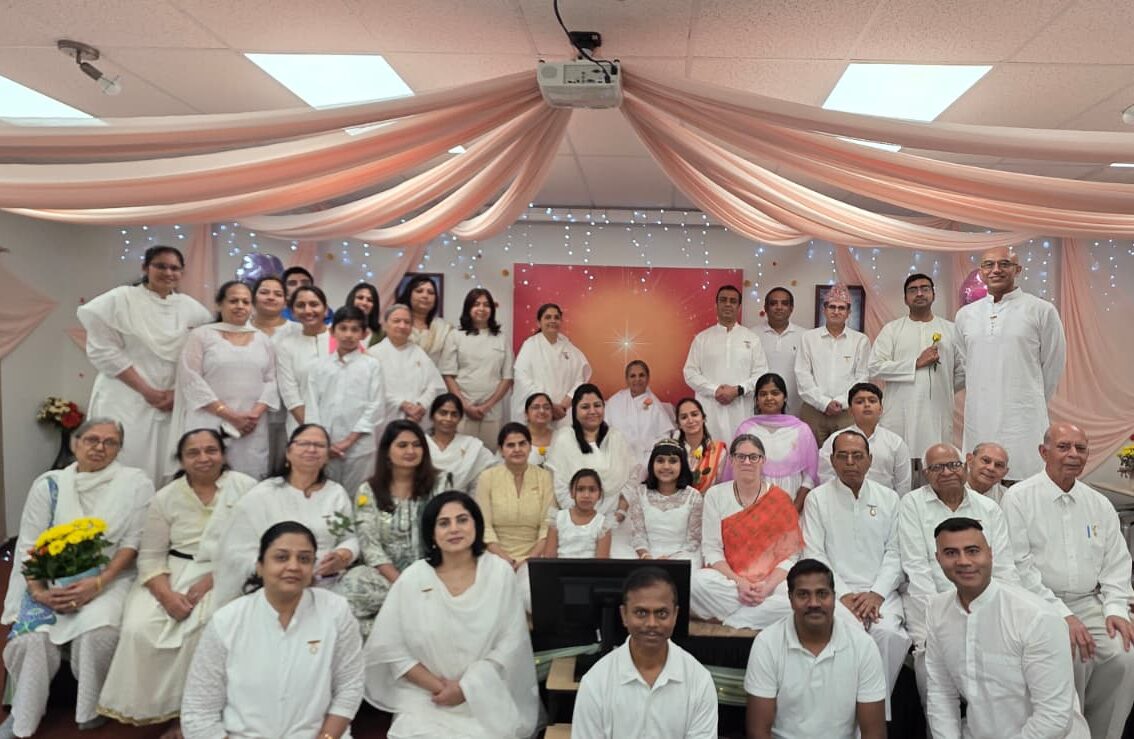 Group of people in white and traditional attire posing indoors with pink drapery and a decorated backdrop.