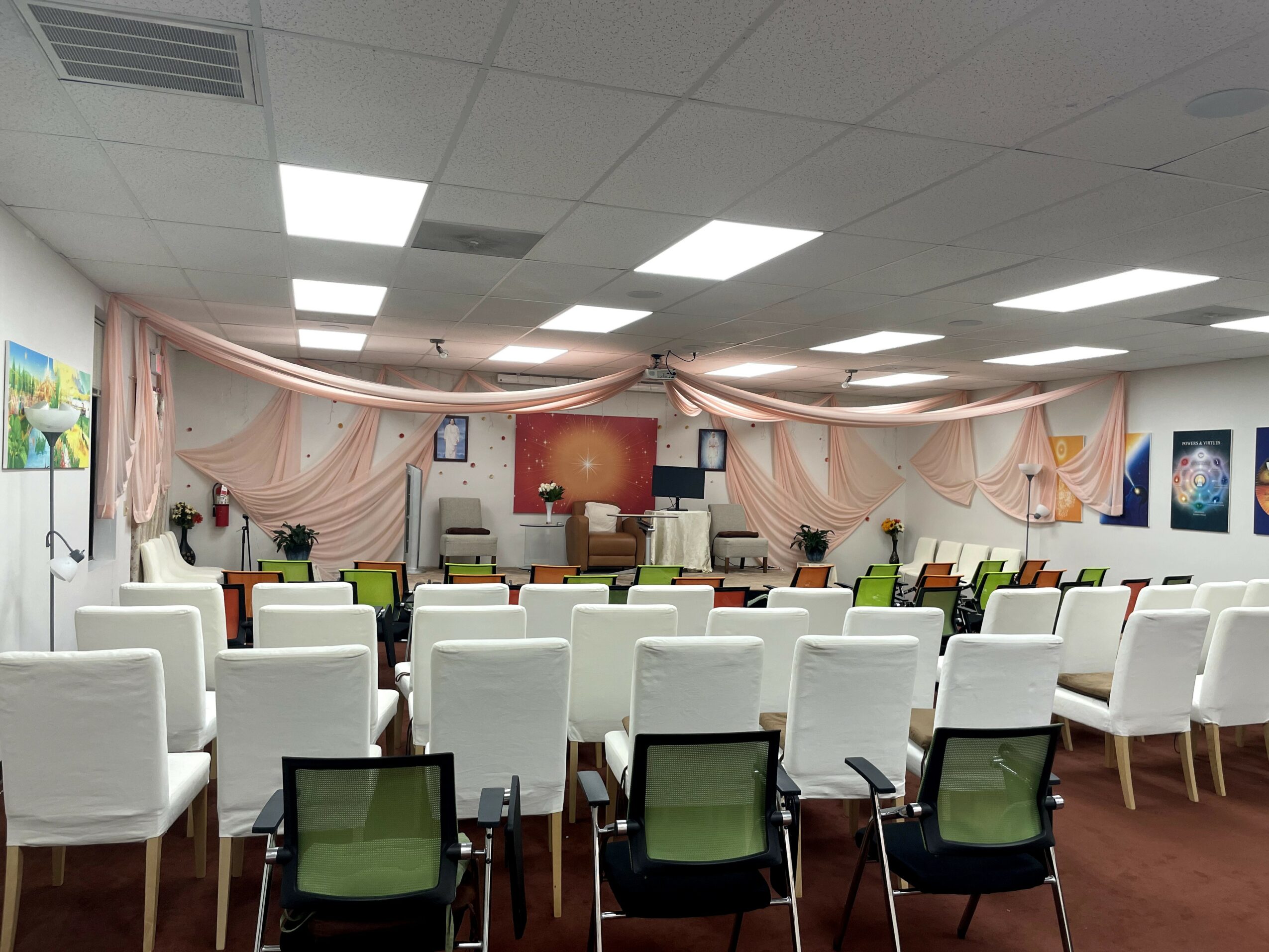 Conference room with chairs facing a stage, decorated with drapes and artwork on walls.