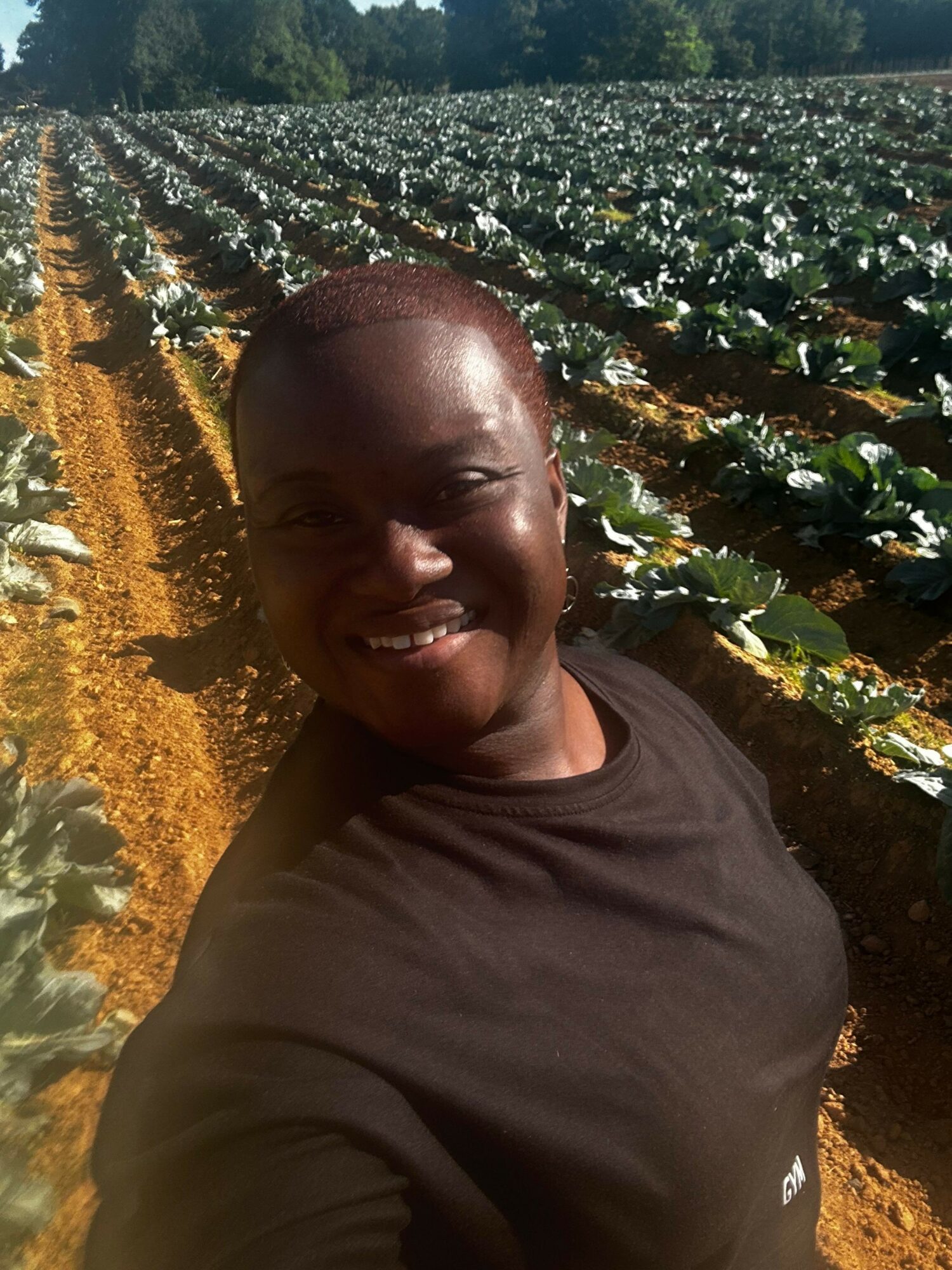 Person smiling outdoors with plants and sunlight in background.