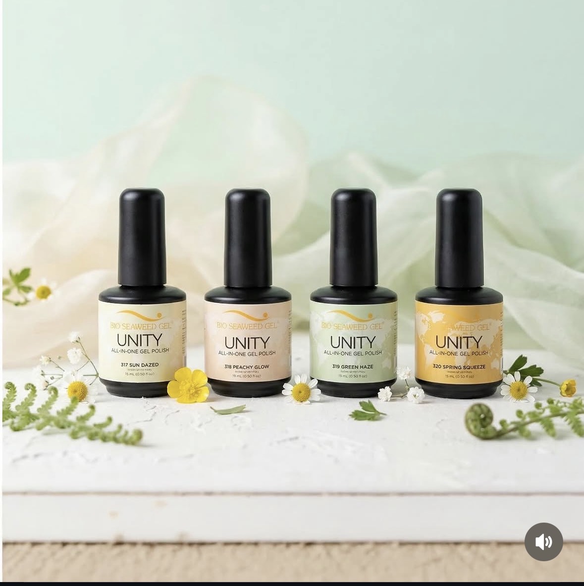 Four bottles of nail polish arranged in a row with small flowers and greenery, light background, flat lay style.