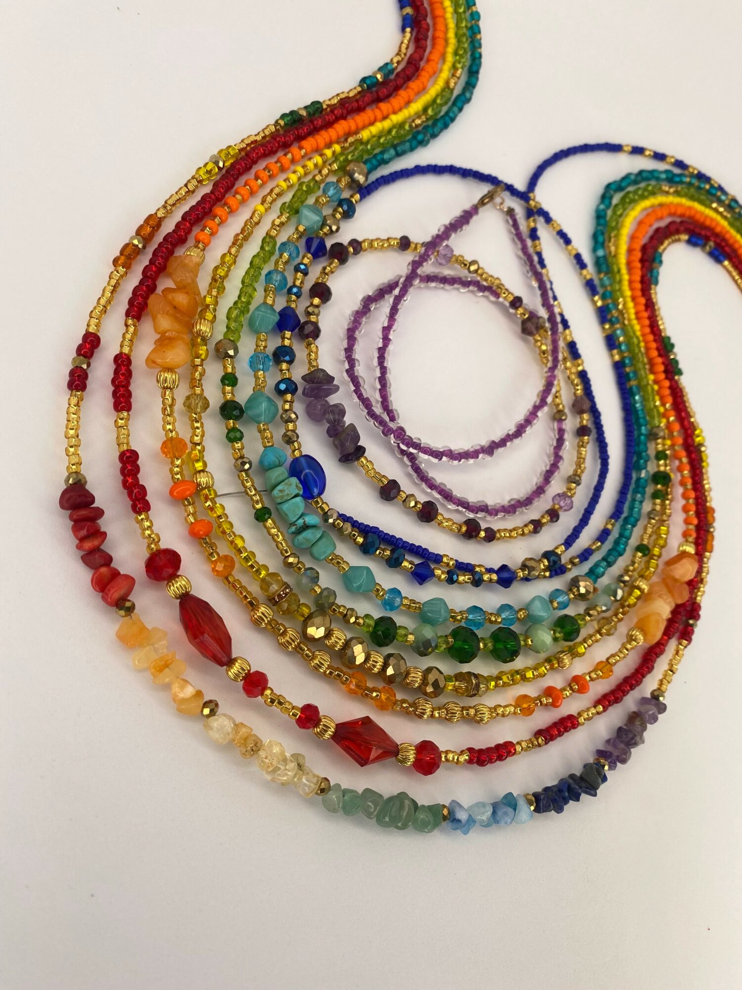 Colorful beaded necklaces arranged in a semi-circle on a white background.