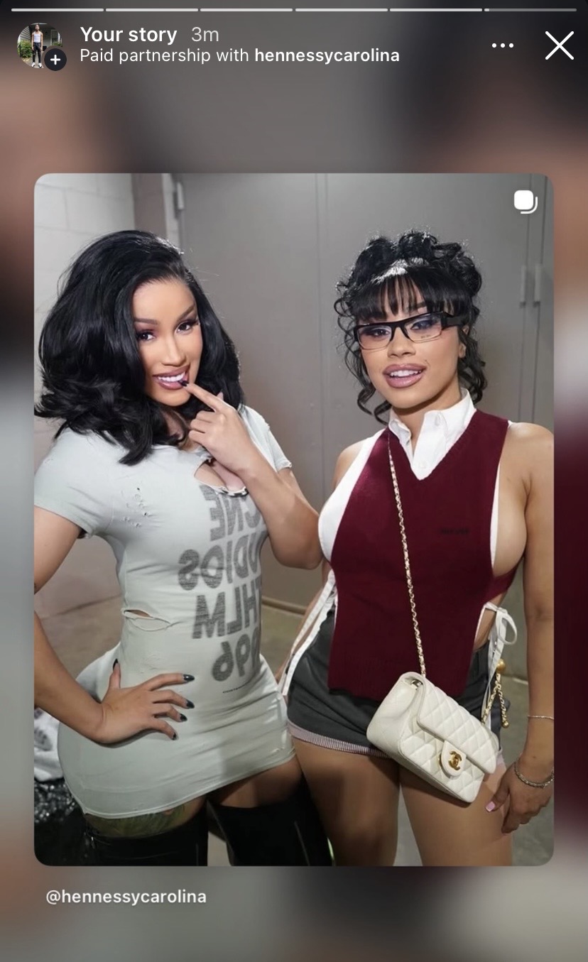 Two women pose together, one with black hair and the other with curly hair and glasses, smiling in a room.