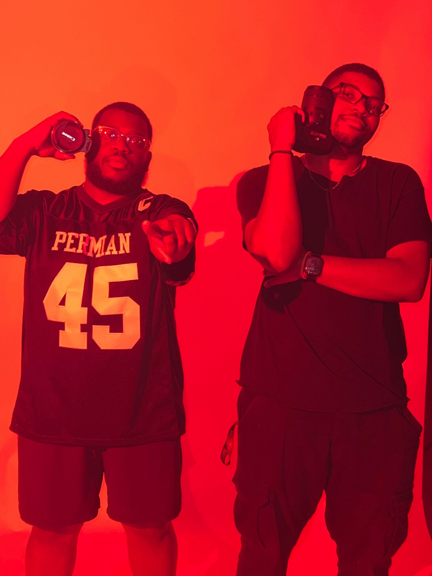 Two people standing, one holding a football, with a red background.