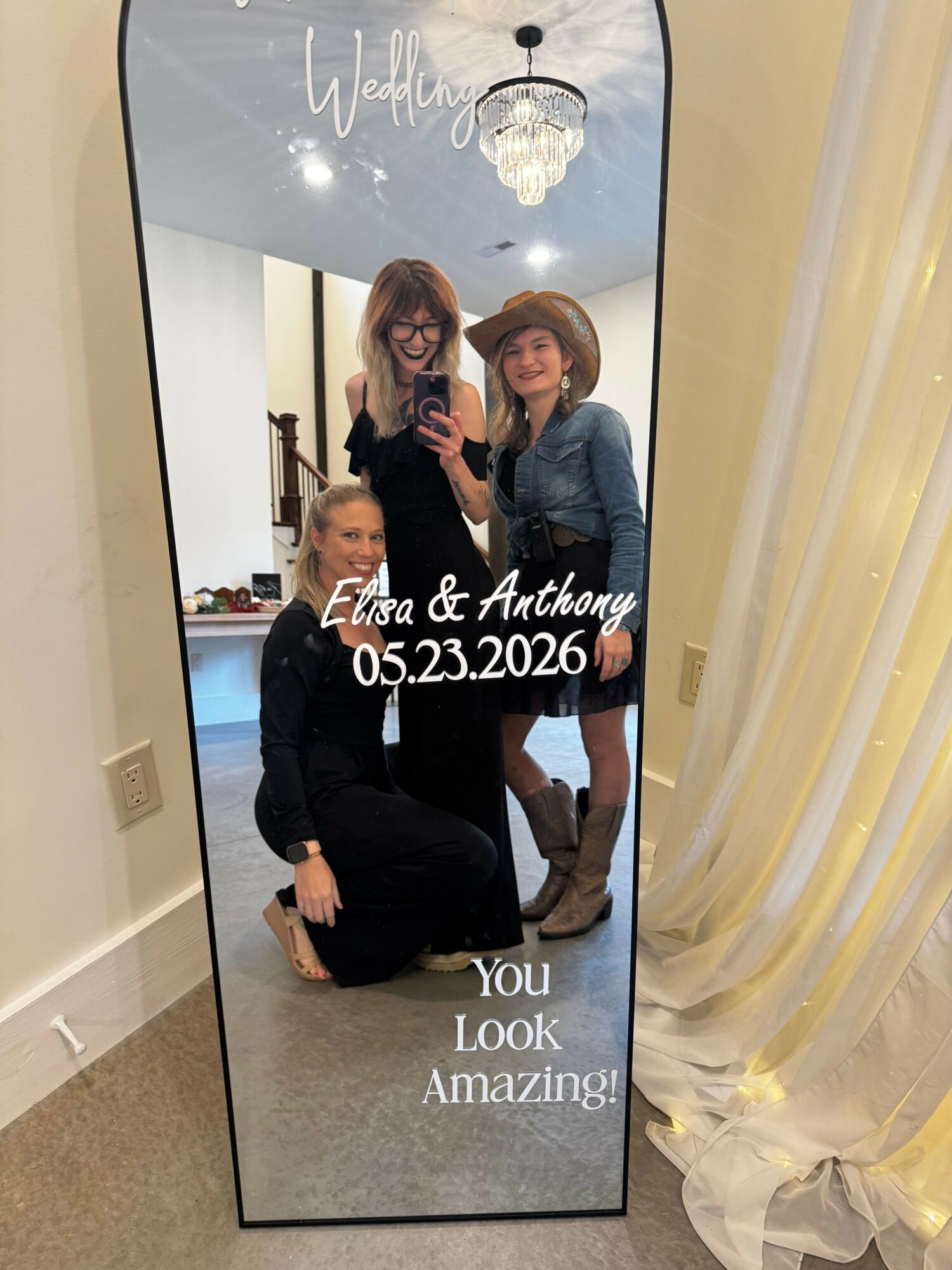 Two women taking a mirror selfie indoors, one sitting on the floor and the other standing, with text overlay. Alt text is 20 words.