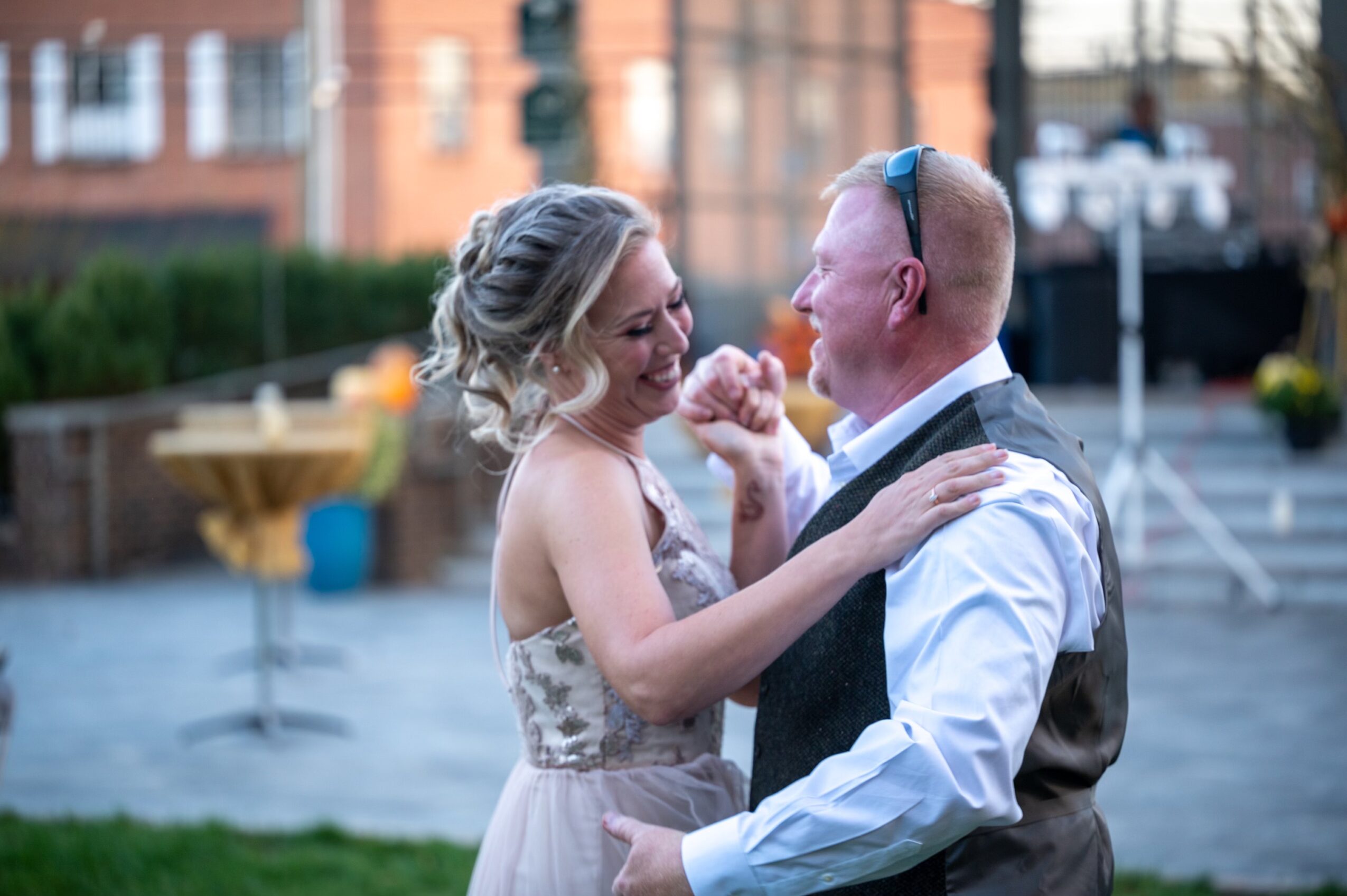 A couple dancing outdoors, smiling, with buildings and trees in the background.