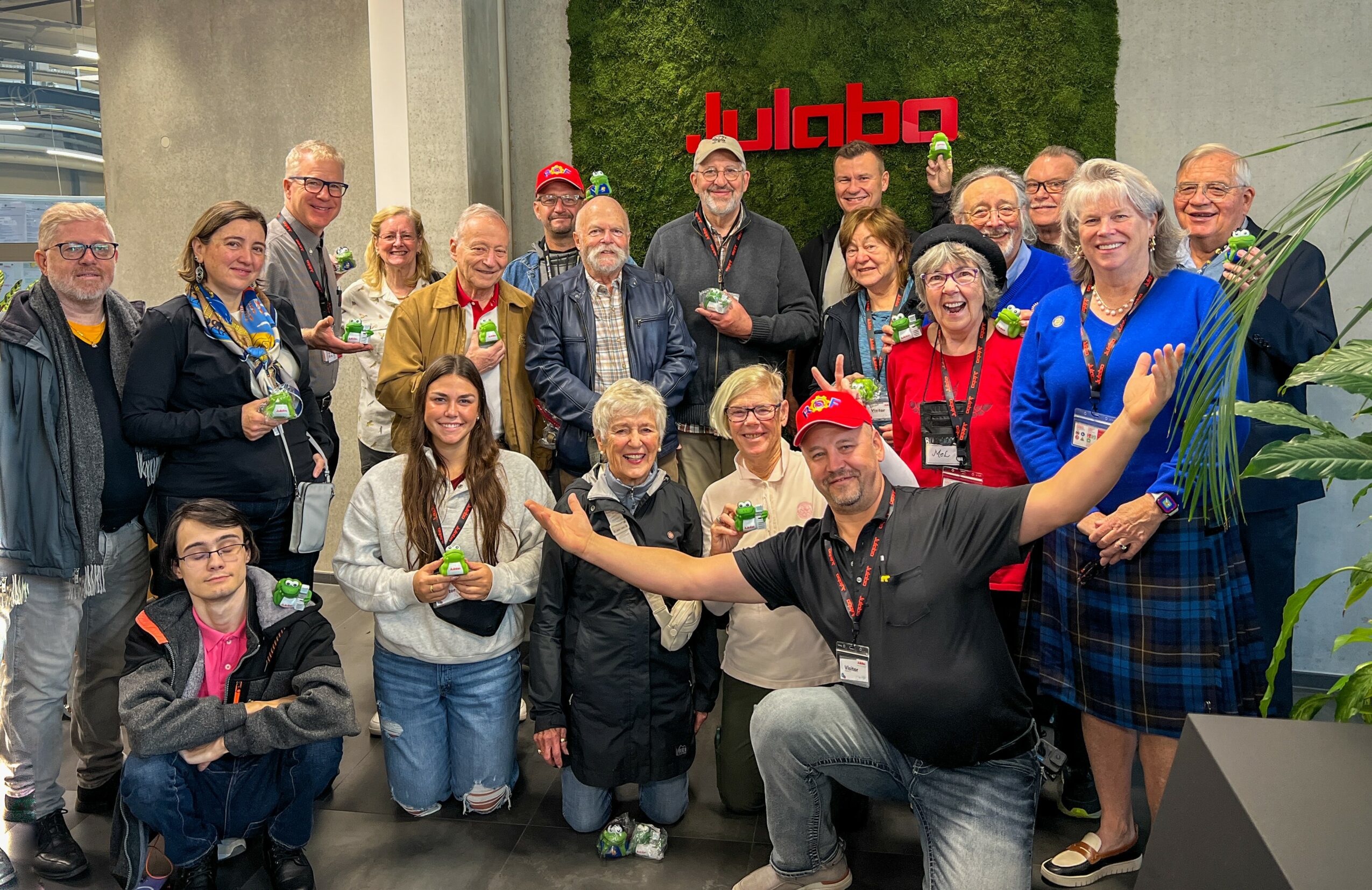 Group of people smiling and posing indoors with a red sign in the background.